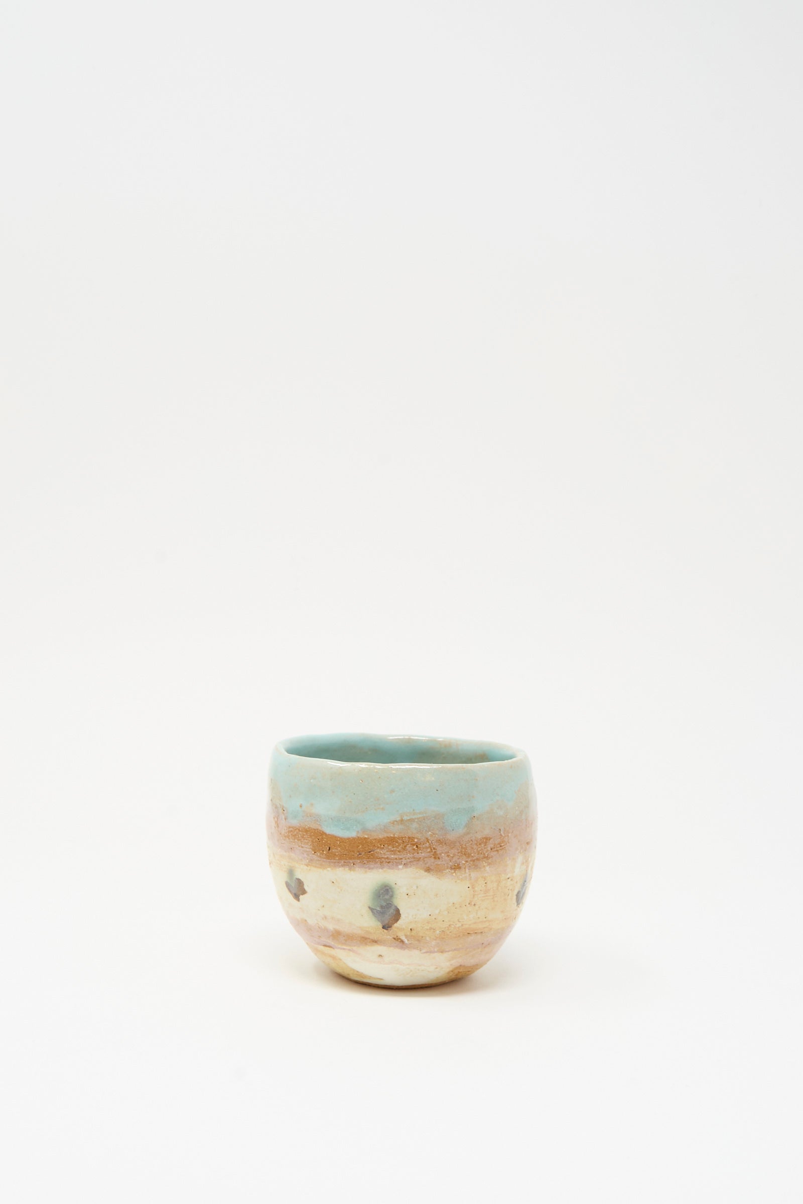 The Cup in Dots II by Shino Takeda is a small, round, hand-painted ceramic cup featuring a mottled beige and brown surface with a light blue rim, shown against a plain white background.