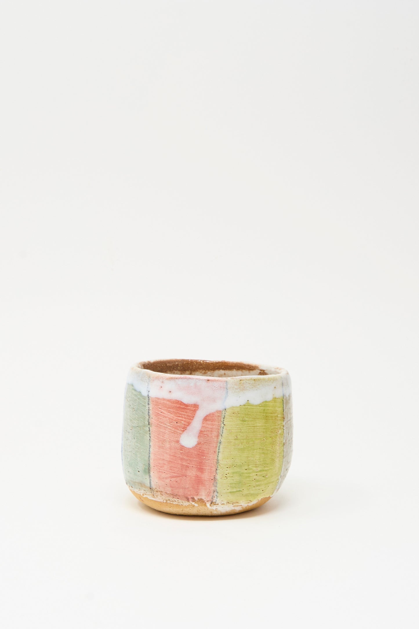 The Cup in Stripe by Shino Takeda is a small hand-painted ceramic cup with vertical pastel pink, green, and beige stripes and a white glaze drip near the rim, crafted in New York and displayed on a plain white background.
