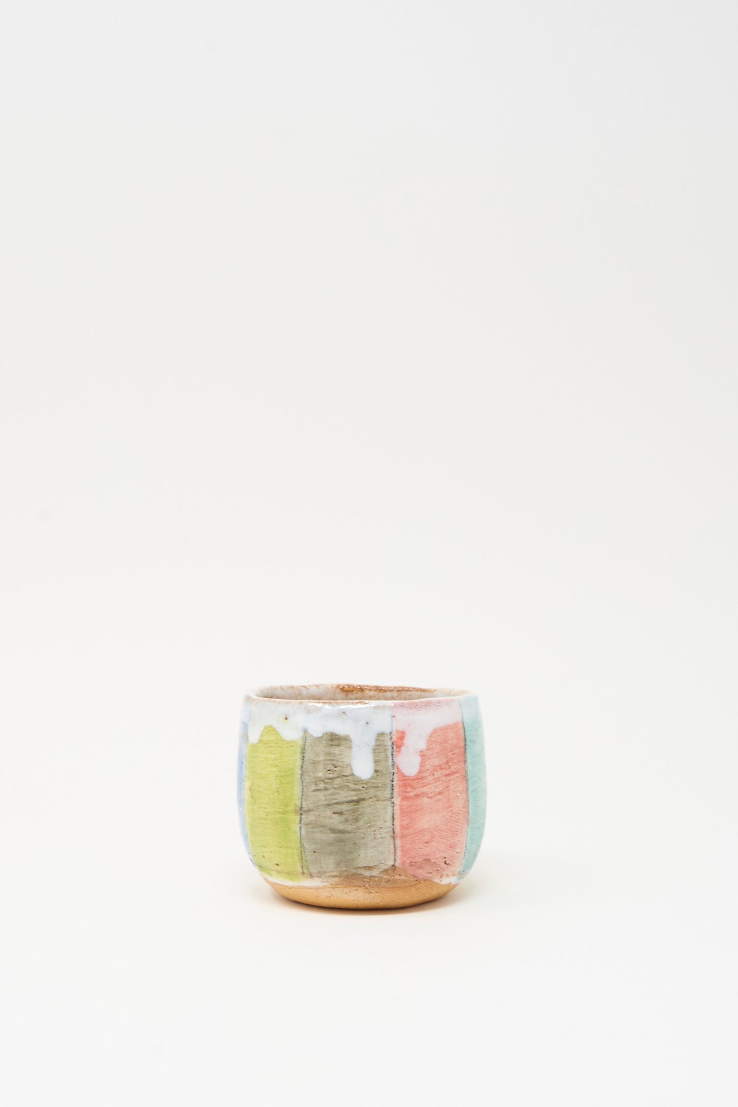 Cup in Stripe I by Shino Takeda is a small hand-painted ceramic pot with a matte finish, vertical pastel stripes, and white glaze dripping from the rim, shown against a plain white background.
