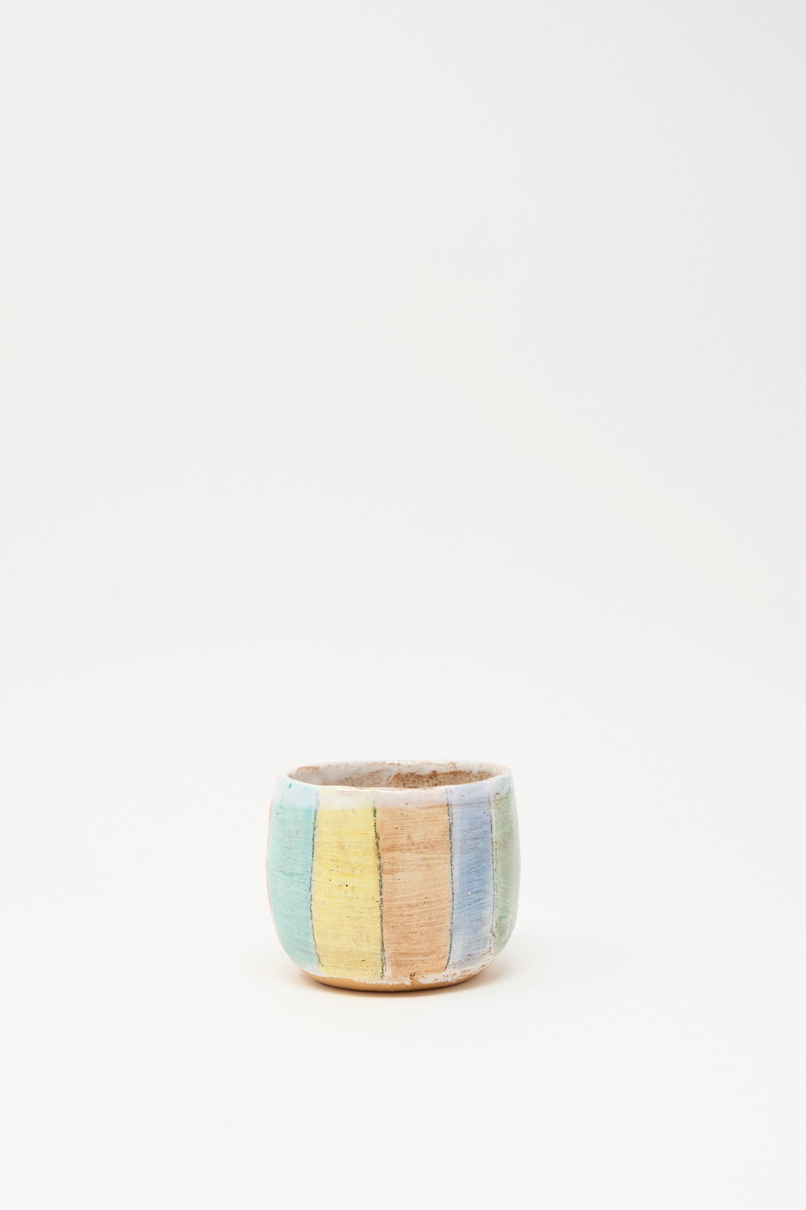 Cup in Stripe I by Shino Takeda is a small ceramic cup featuring a rough texture and hand-painted vertical pastel stripes in yellow, blue, green, and pink, displayed on a plain white background.