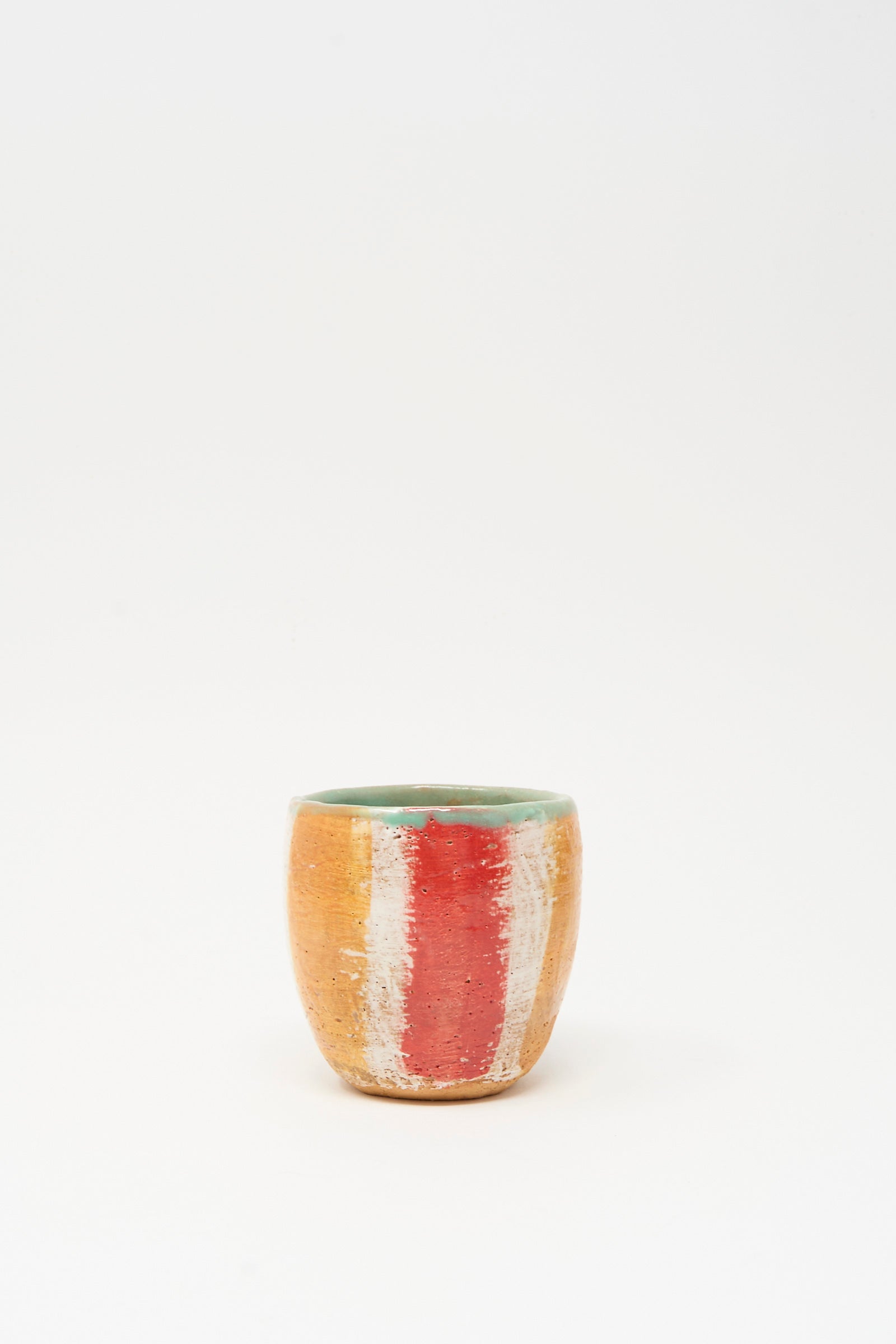 Cup in Stripe II by Shino Takeda is a small hand-painted ceramic cup with a green interior and orange exterior, adorned with vertical red and white stripes, shown on a plain white background.