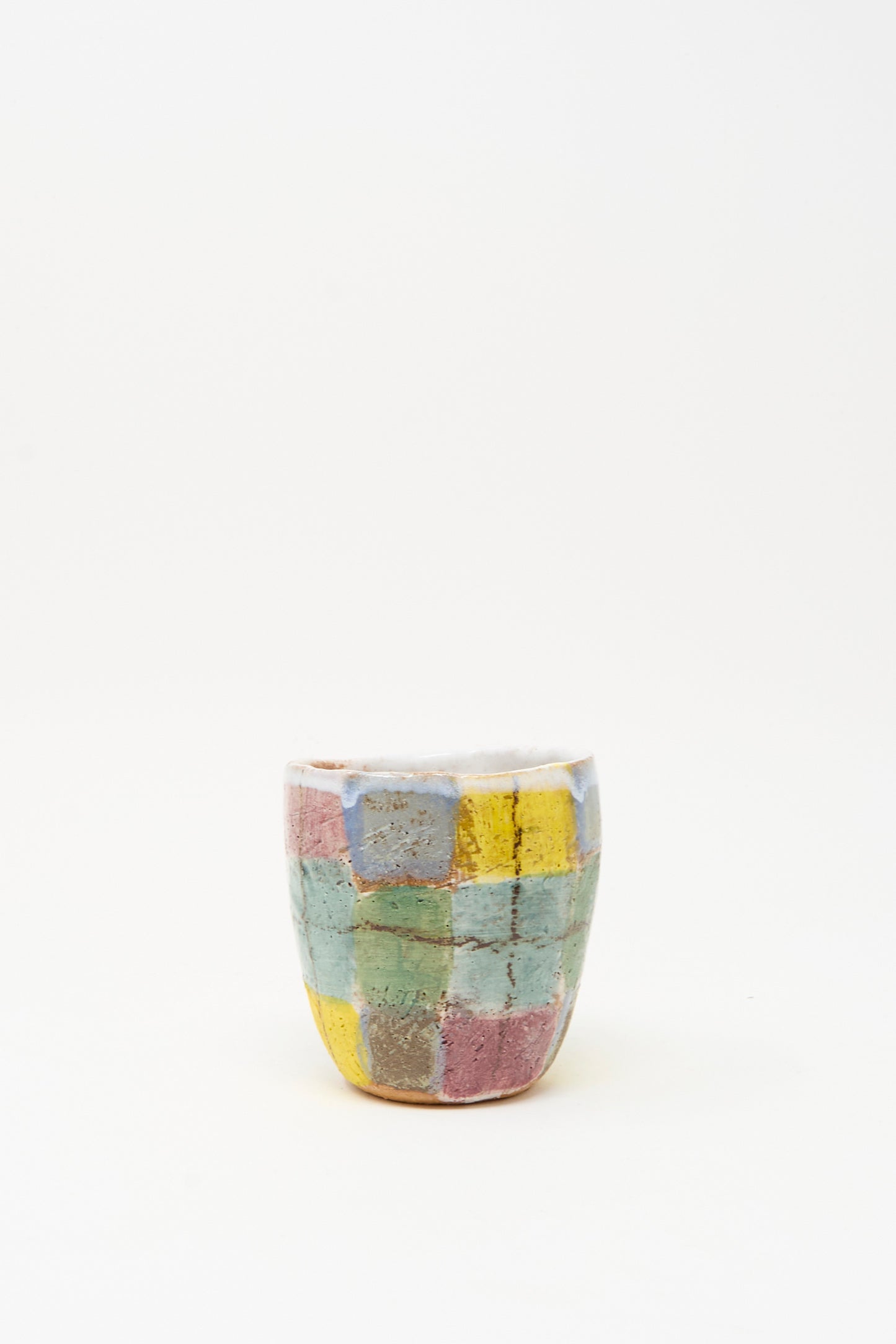 The Cup in Blue Plaid by Shino Takeda is a small, handmade ceramic cup from New York, featuring a hand-painted patchwork of pastel yellow, pink, blue, and green squares on white.
