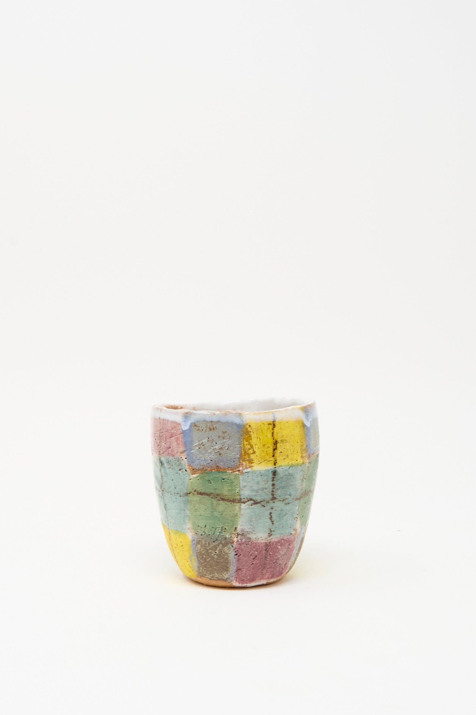 The Cup in Blue Plaid by Shino Takeda is a small, handmade ceramic cup from New York, featuring a hand-painted patchwork of pastel yellow, pink, blue, and green squares on white.