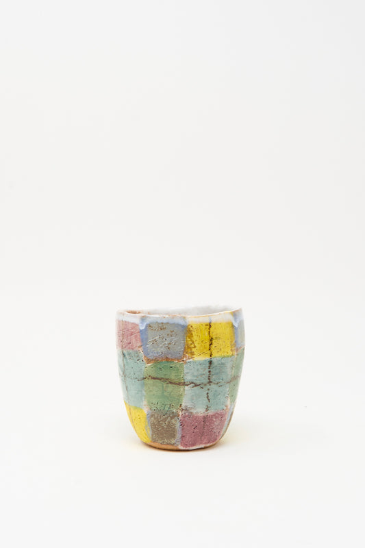 The Cup in Blue Plaid by Shino Takeda is a small, handmade ceramic cup from New York, featuring a hand-painted patchwork of pastel yellow, pink, blue, and green squares on white.