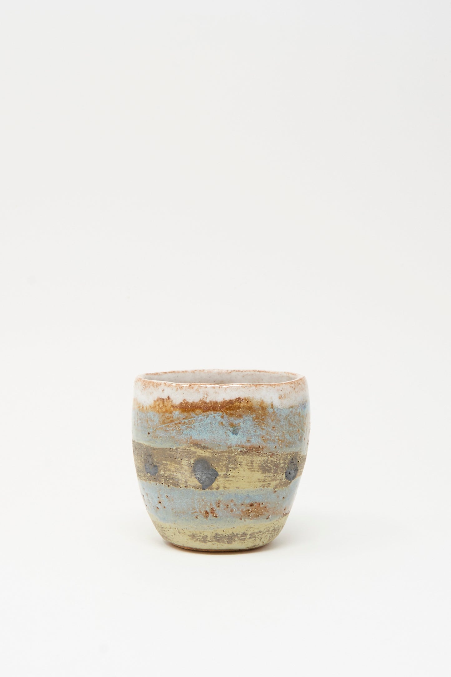 The Cup Tall in Dots I by Shino Takeda is a small, round ceramic with hand-painted dots and a textured, rustic surface, crafted in New York and set against a plain white background.