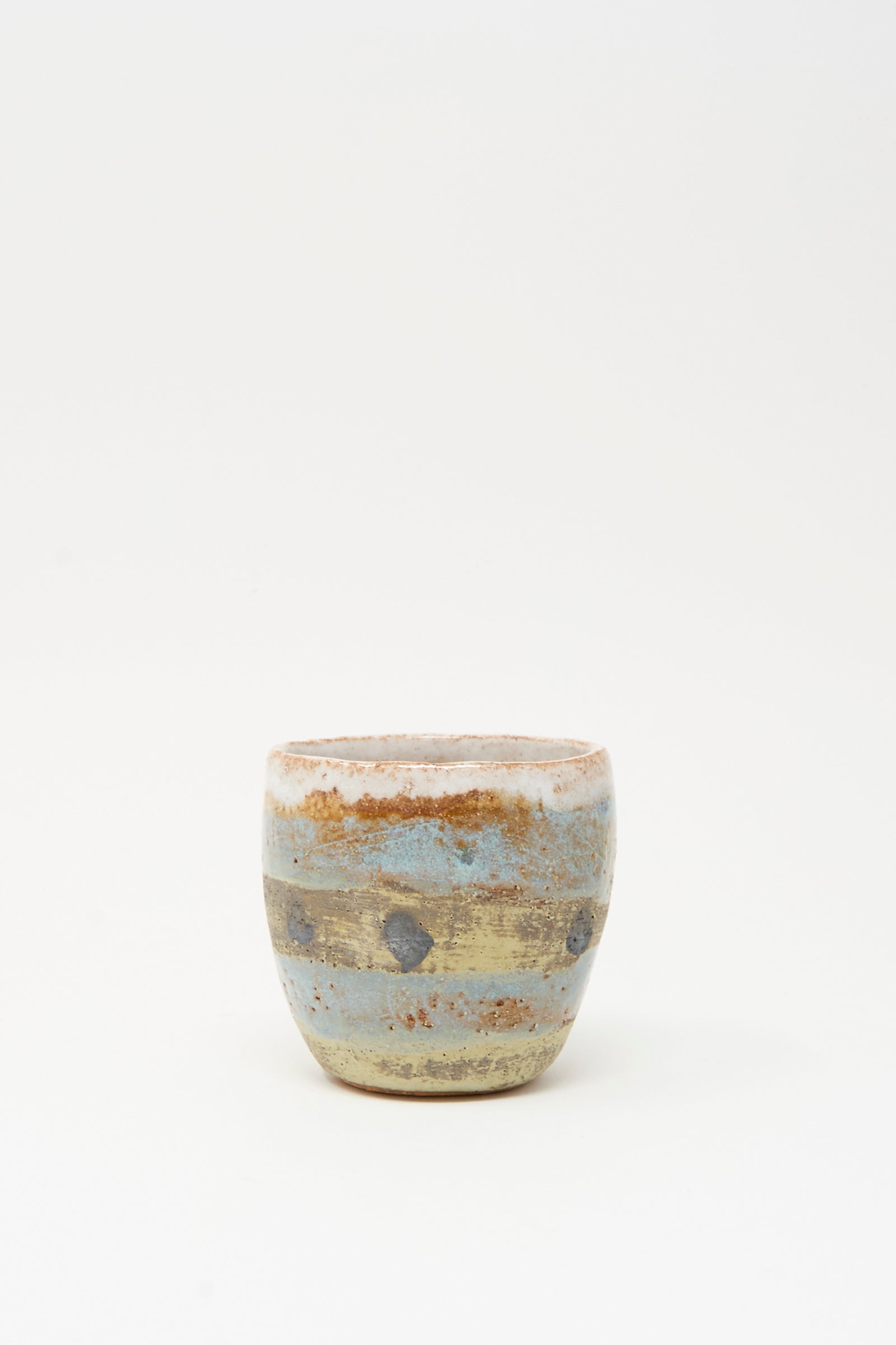 The Cup Tall in Dots I by Shino Takeda is a small, round ceramic with hand-painted dots and a textured, rustic surface, crafted in New York and set against a plain white background.