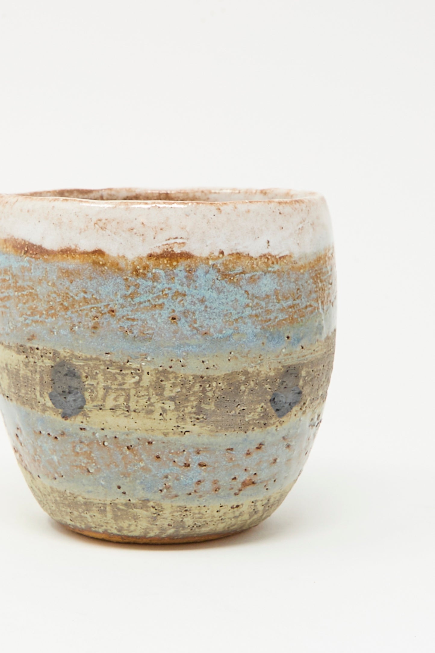 The Cup Tall in Dots I by Shino Takeda is a handmade ceramic cup with a rough texture and layered earth-toned glazes, featuring hand-painted dots in beige, brown, blue, and gray. Made in New York, shown against a plain white background.