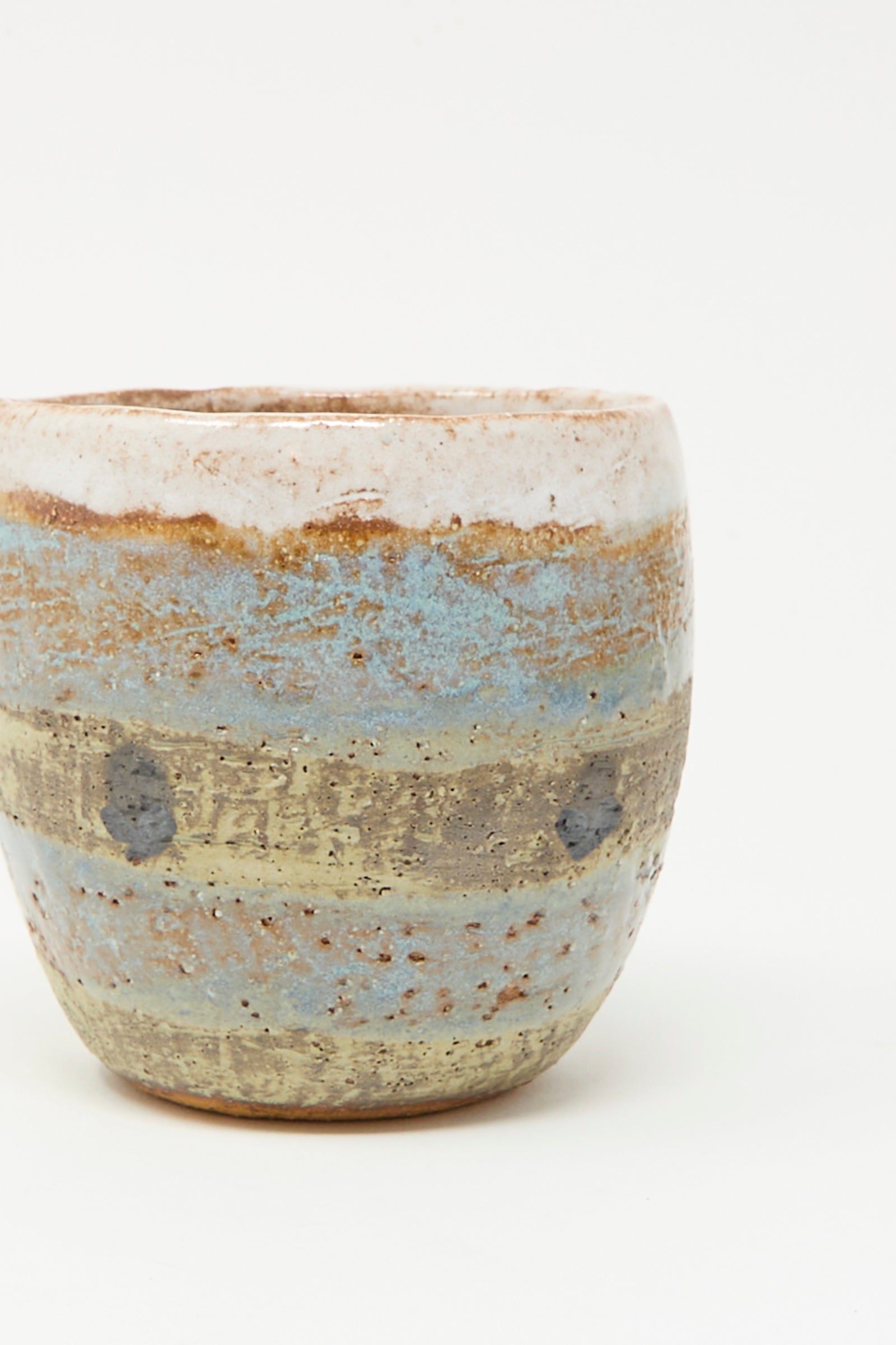 The Cup Tall in Dots I by Shino Takeda is a handmade ceramic cup with a rough texture and layered earth-toned glazes, featuring hand-painted dots in beige, brown, blue, and gray. Made in New York, shown against a plain white background.