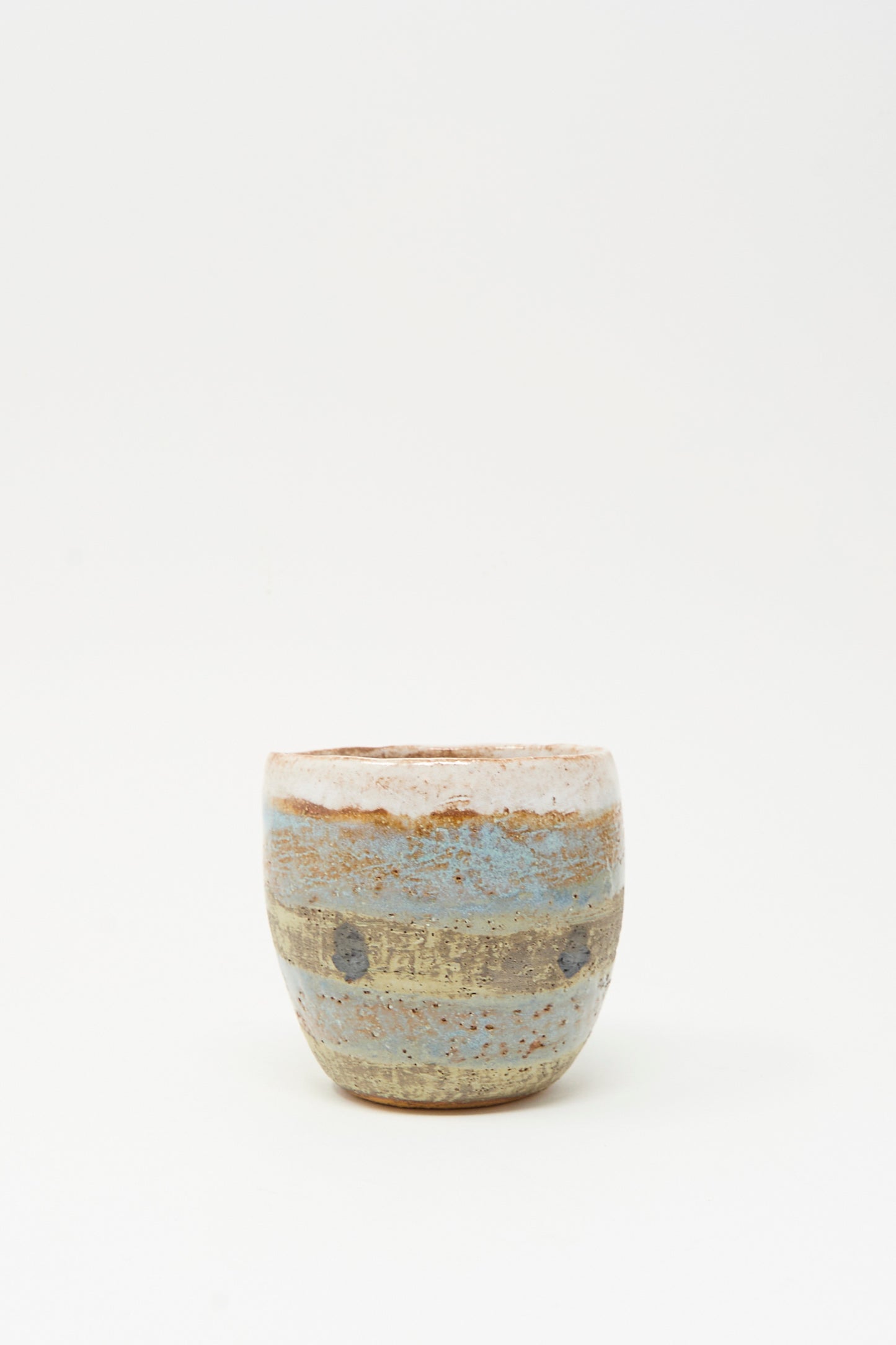 The Cup Tall in Dots I by Shino Takeda is a small, round ceramic cup, hand-painted with earthy brown, beige, and blue horizontal stripes, shown on a plain white background.