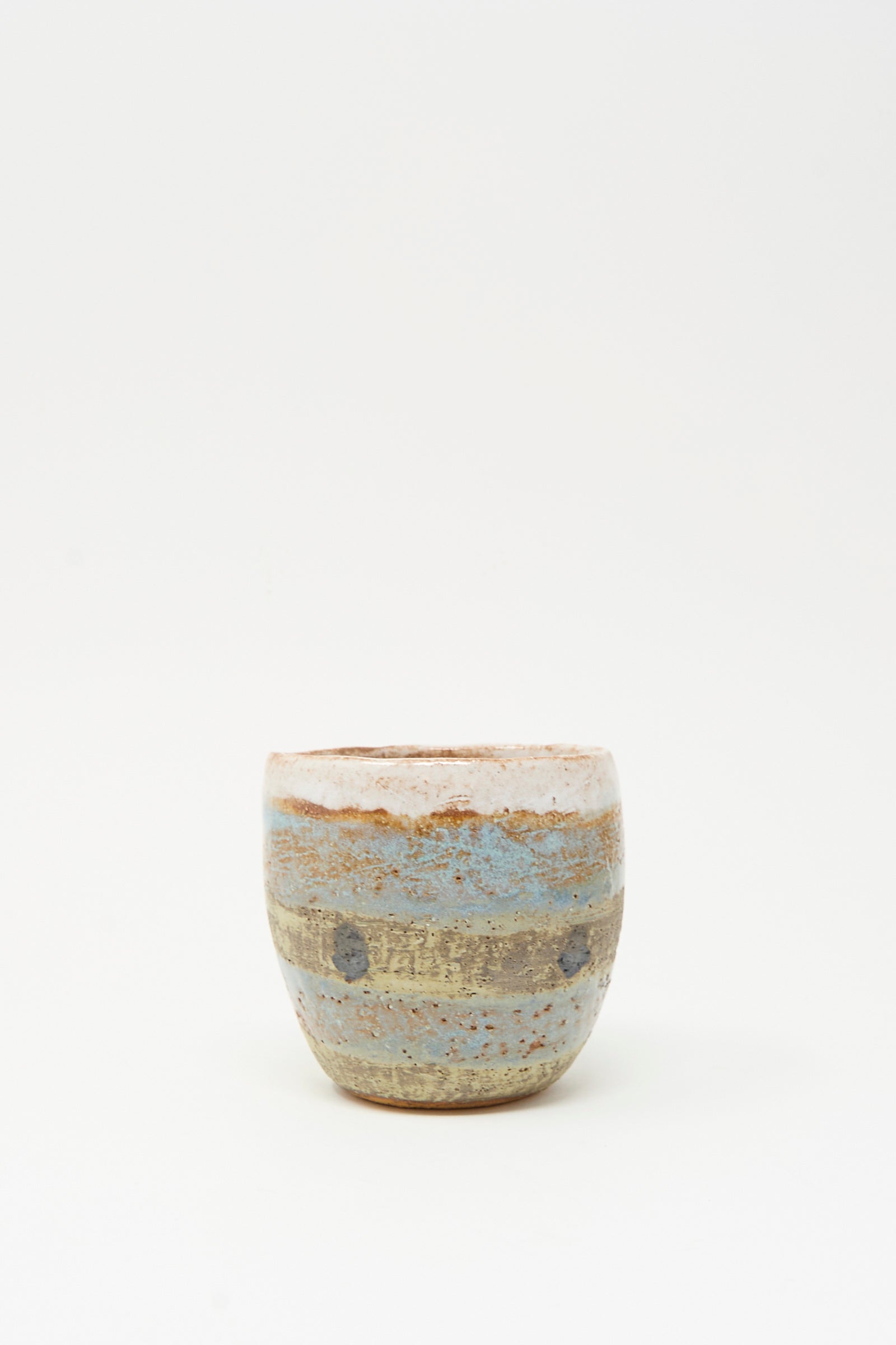The Cup Tall in Dots I by Shino Takeda is a small, round ceramic cup, hand-painted with earthy brown, beige, and blue horizontal stripes, shown on a plain white background.