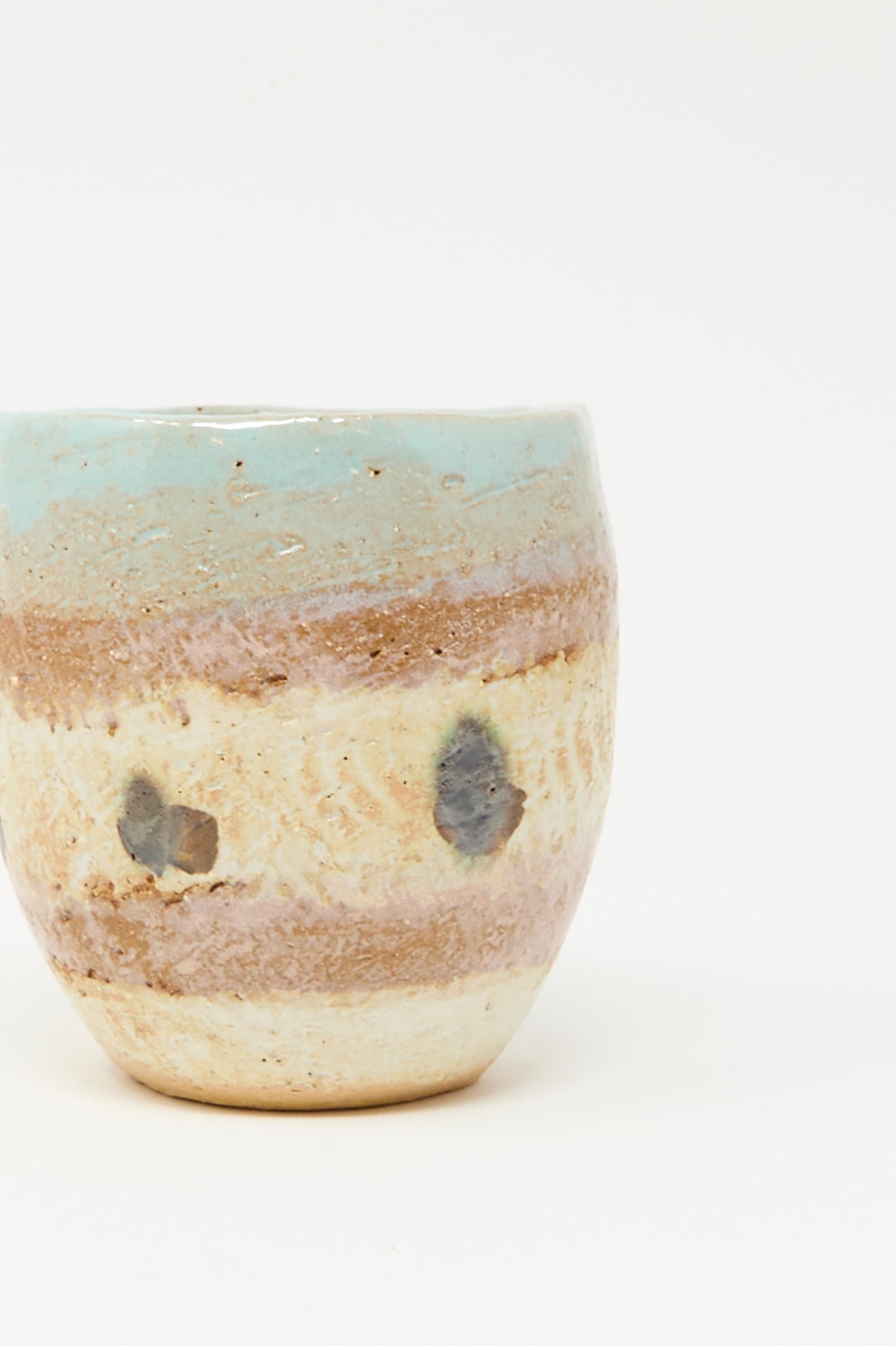 The Cup Tall in Dots II by Shino Takeda is a handmade ceramic cup with a rounded shape, crafted in New York. It features layered beige, brown, and light blue glaze with two dark spots, shown on a plain white background.