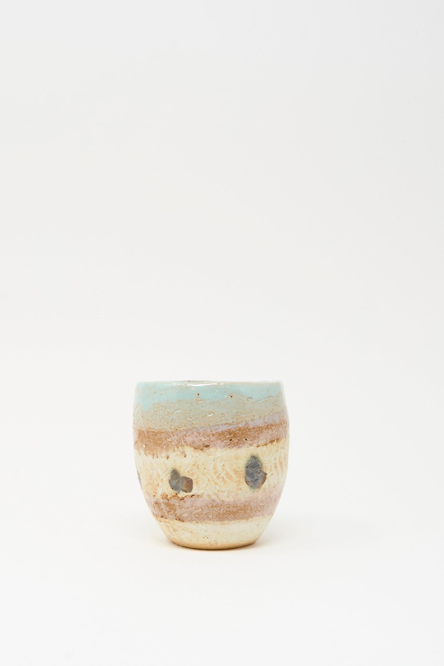 The Cup Tall in Dots II by Shino Takeda is a small, hand-painted ceramic cup with a rounded shape, earthy brown and beige tones, and a light blue top rim, shown on a plain white background.