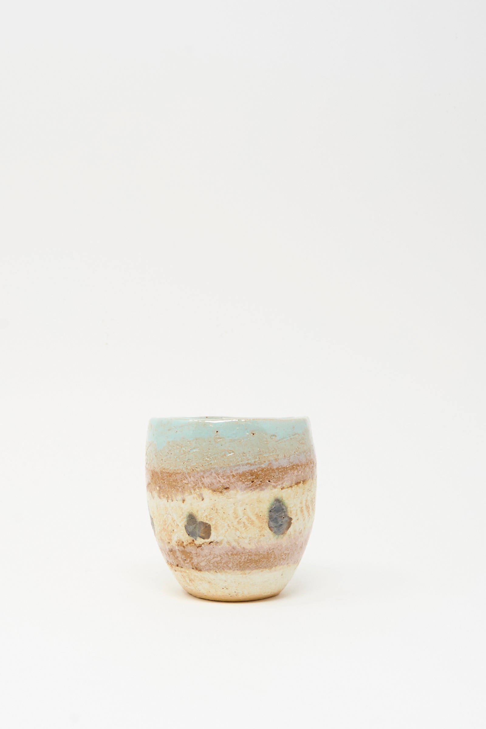 The Cup Tall in Dots II by Shino Takeda is a small, hand-painted ceramic cup with a rounded shape, earthy brown and beige tones, and a light blue top rim, shown on a plain white background.