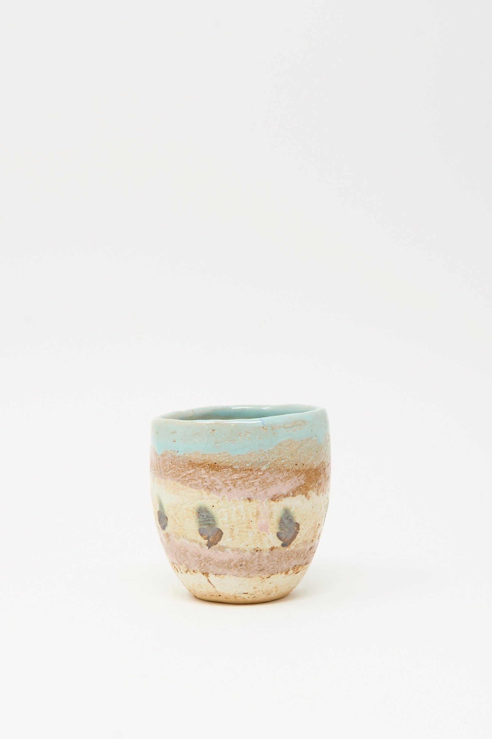 The Cup Tall in Dots II by Shino Takeda is a small, hand-painted ceramic cup with a rounded shape, light blue rim, earthy beige and brown hues, and dark speckled dots.