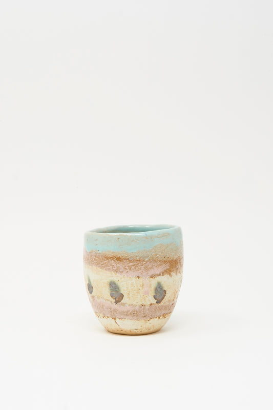 The Cup Tall in Dots II by Shino Takeda is a small, hand-painted ceramic cup with a rounded shape, light blue rim, earthy beige and brown hues, and dark speckled dots.