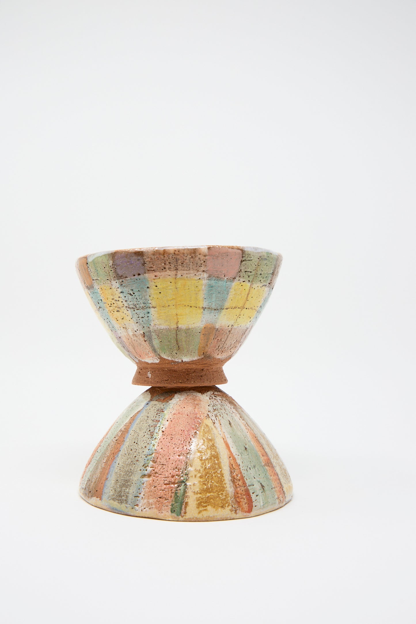 A hand-painted "Footed Bowl in Pastel Stripe" by Shino Takeda, showcasing a variety of colors with a rustic finish, is upside down below another bowl against a plain background.