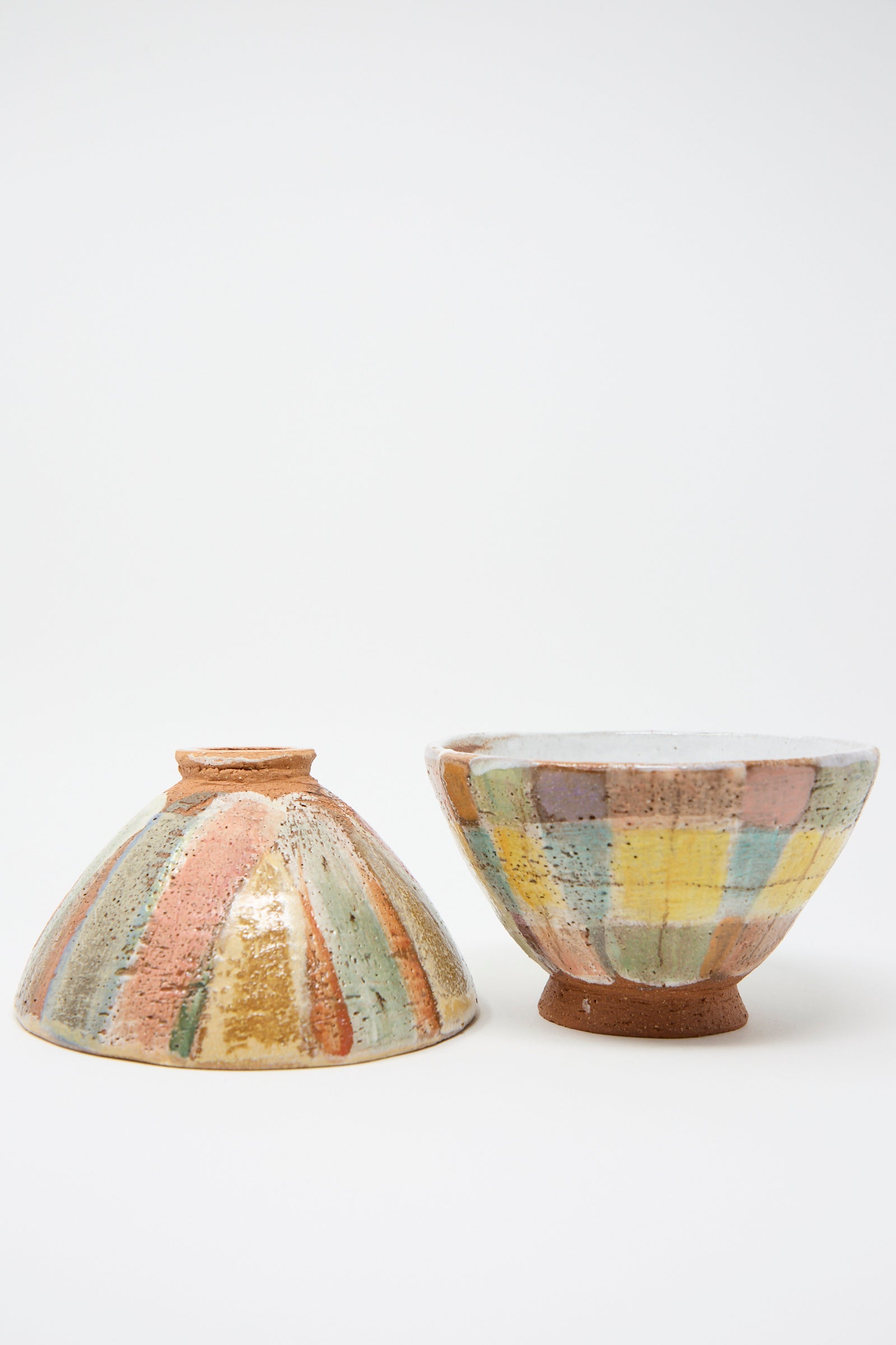 The Footed Bowl in Pastel Stripe by Shino Takeda features soft multicolored striped patterns and is shown upside down alongside another plaid bowl.