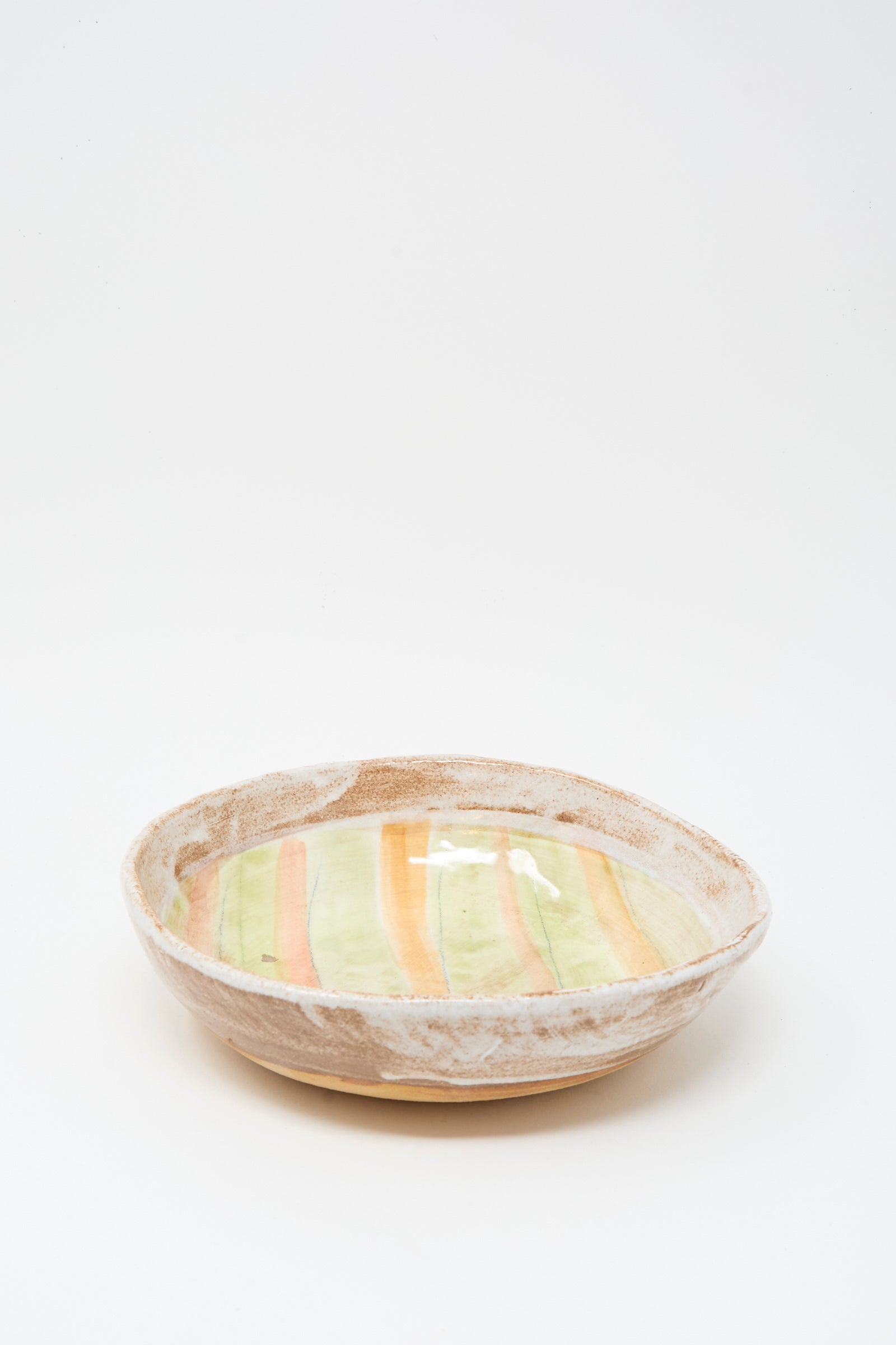 The Serving Bowl in Stripes by Shino Takeda is a handmade ceramic bowl with a textured earthy rim and glazed interior featuring vertical yellow and orange stripes.