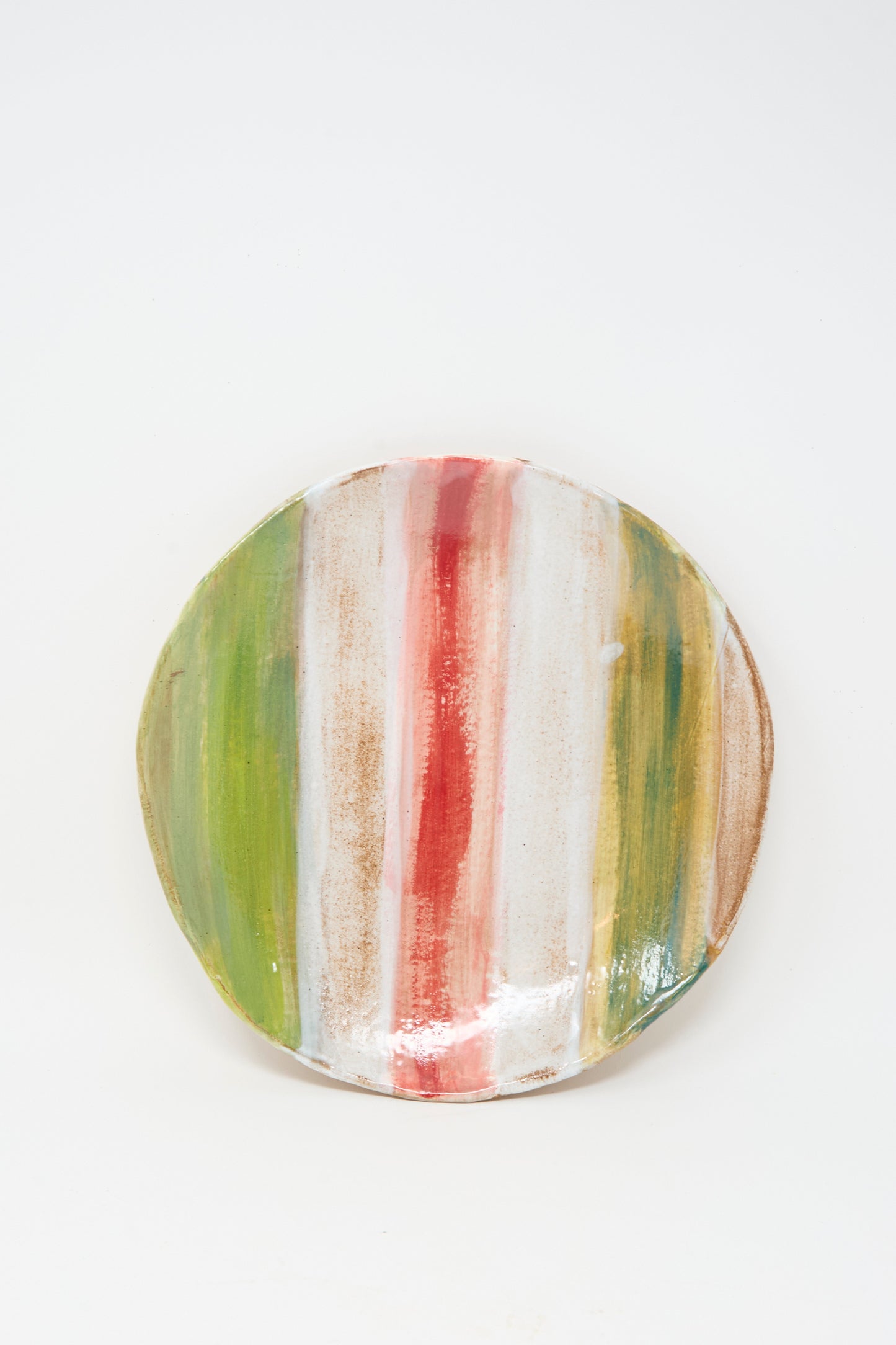 The Serving Plate in Red Green Stripe by Shino Takeda features handmade ceramic craftsmanship with vertical stripes in green, red, and brown on a crisp white background.
