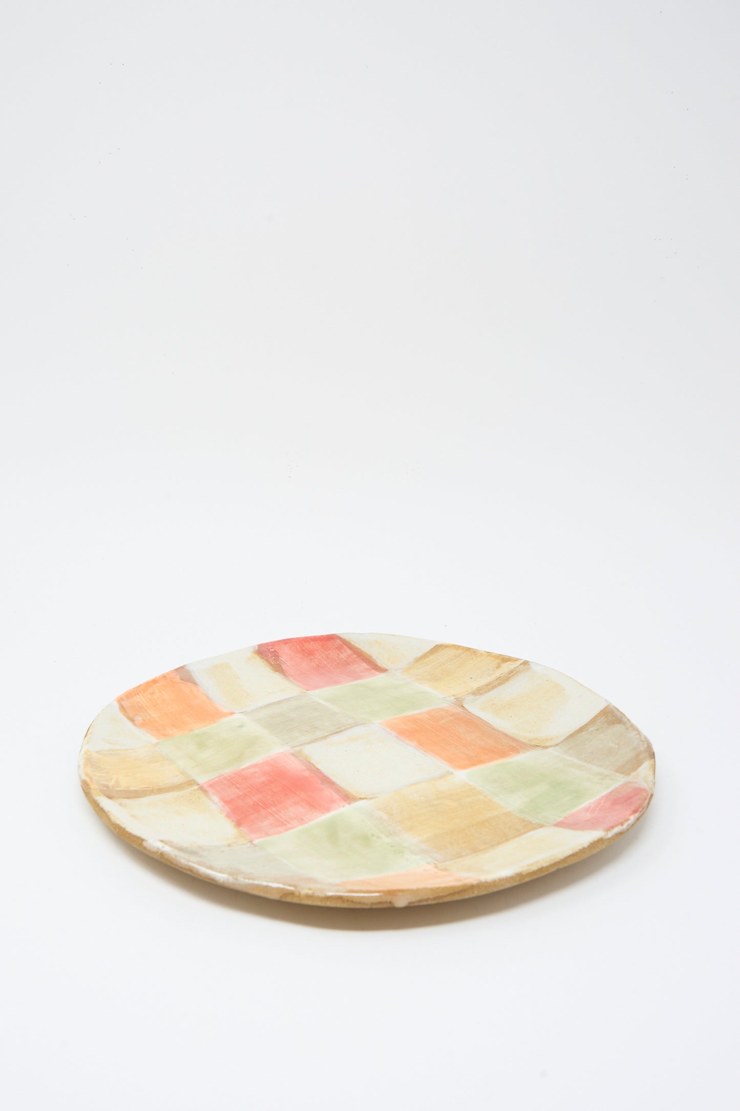 The Serving Plate in Squares by Shino Takeda is a handmade ceramic plate with a colorful wash of pastel red, yellow, green, and beige checks on a white background.