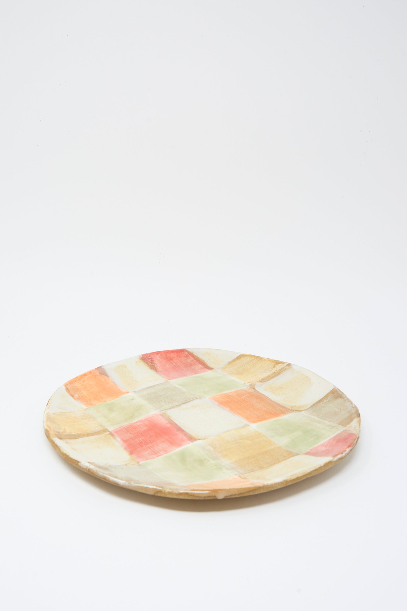 The Serving Plate in Squares by Shino Takeda is a handmade ceramic plate with a colorful wash of pastel red, yellow, green, and beige checks on a white background.