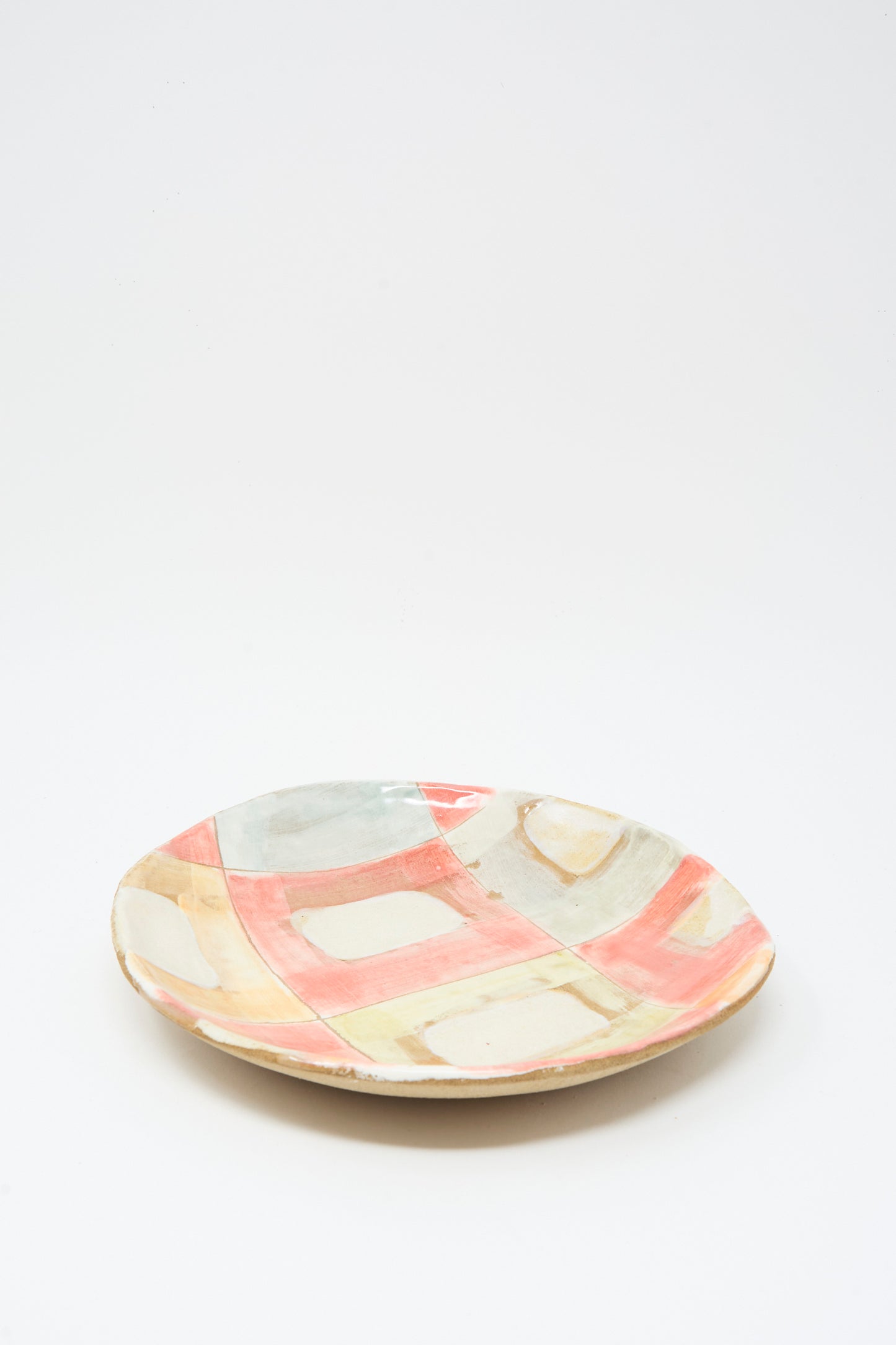 The Shino Takeda Serving Shallow Plate in Squares is a handmade ceramic plate from New York, featuring pastel geometric patterns and colorful pink, blue, yellow, and beige check washes on a plain white background.