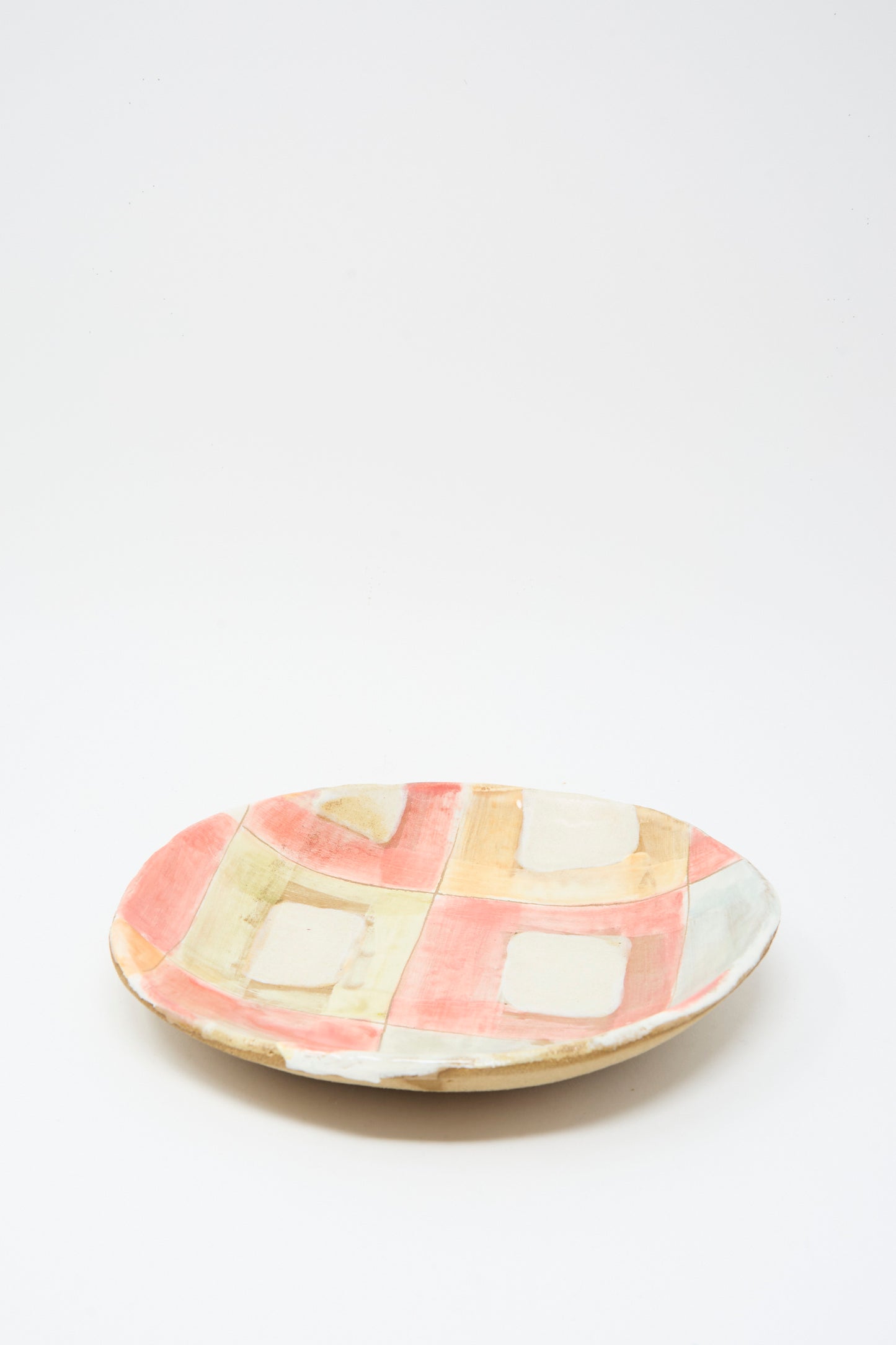 The Serving Shallow Plate in Squares by Shino Takeda is a handmade New York ceramic plate with pink, beige, and green pastel geometric squares and rectangles over a plain white background.