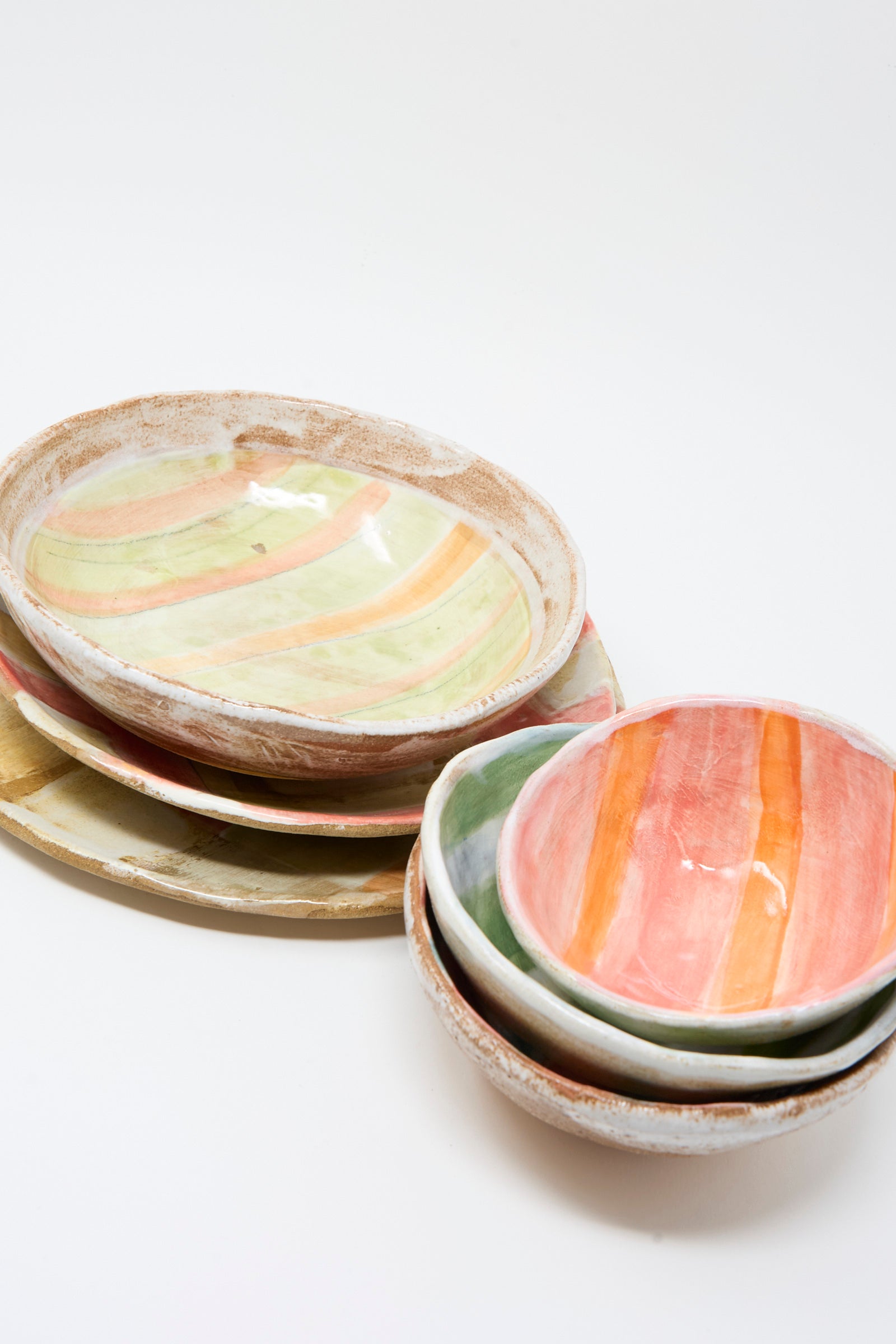 A stack of Shino Takeda Serving Shallow Plates in Squares features handmade New York ceramics with pastel stripes and colorful check patterns, set against a white background.