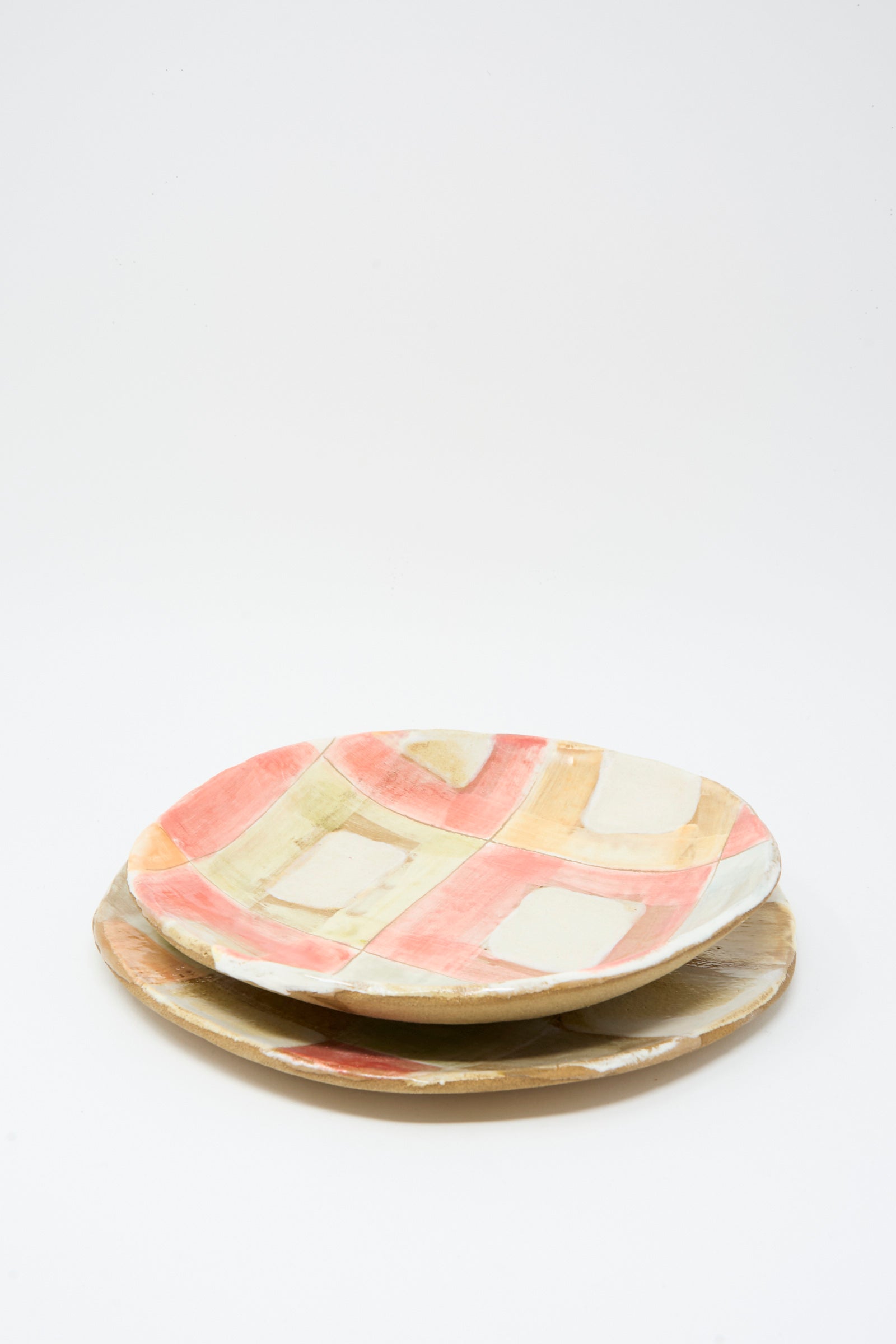 Two Shino Takeda Serving Shallow Plates in Squares, handmade in New York with geometric patterns in muted red, beige, and white, are stacked on a plain white background.