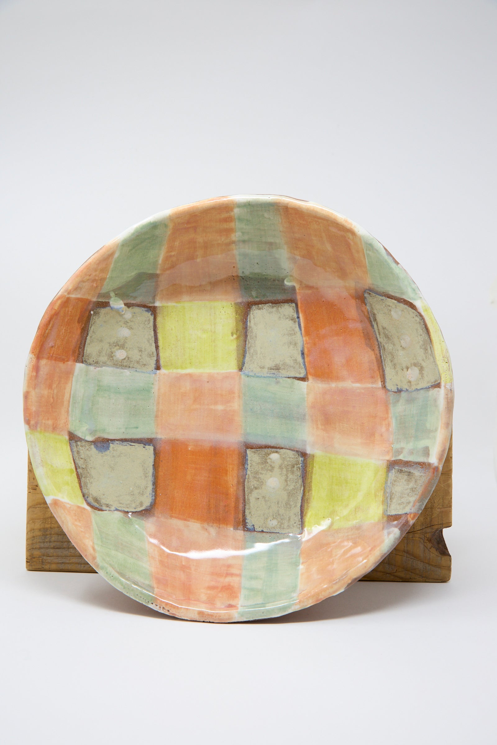 The Shallow Bowl in Pastel Checker by Shino Takeda, featuring a hand-painted multicolored plaid design with shades of orange, green, and beige, is standing against a plain background.