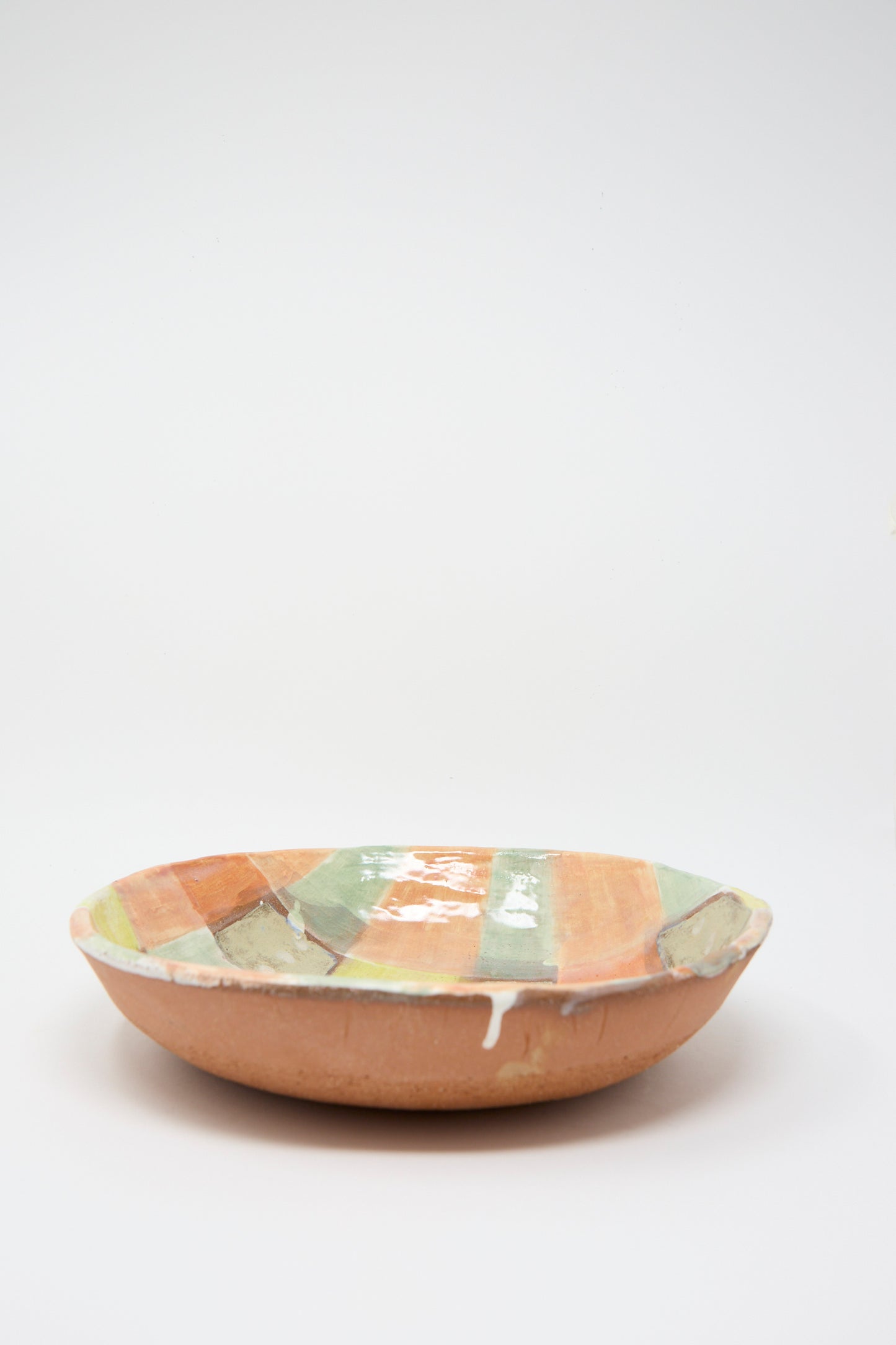 The Shino Takeda Shallow Bowl in Pastel Checker, featuring a hand-painted plaid design in earthy tones of orange, green, and beige, is showcased against a plain white background.