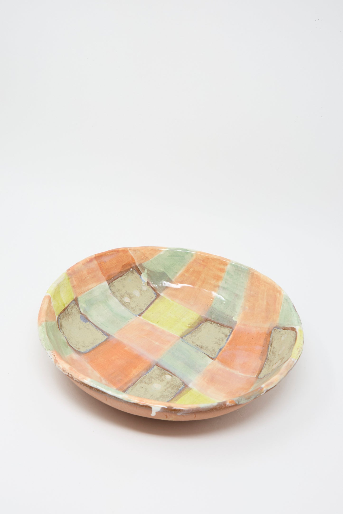 The Shino Takeda Shallow Bowl in Pastel Checker is a hand-painted ceramic bowl in a colorful checkered pattern in orange, green, yellow, and gray tones on a white background.