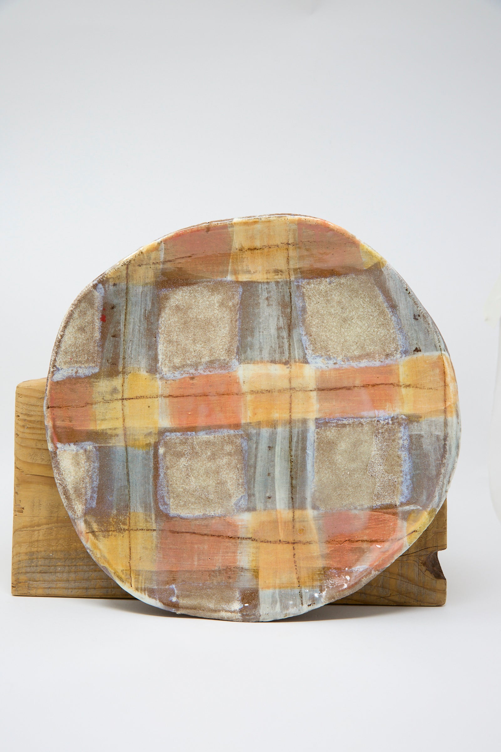 The Shino Takeda Shallow Plate in Pastel Plaid, featuring hand-painted ceramic in orange, beige, and gray tones, is standing on a wooden surface.