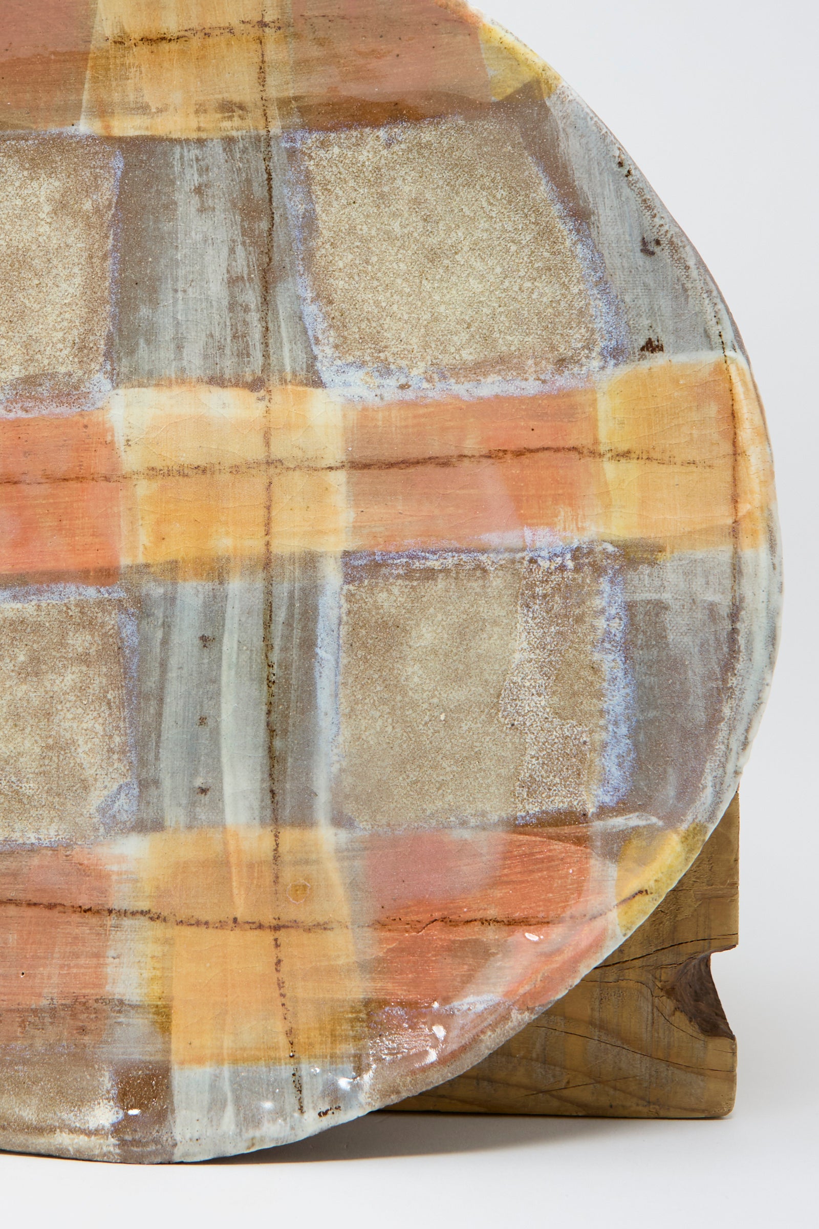 A close up of Shino Takeda's Shallow Plate in Pastel Plaid, featuring a plaid pattern in earthy tones, is placed against a wooden surface.