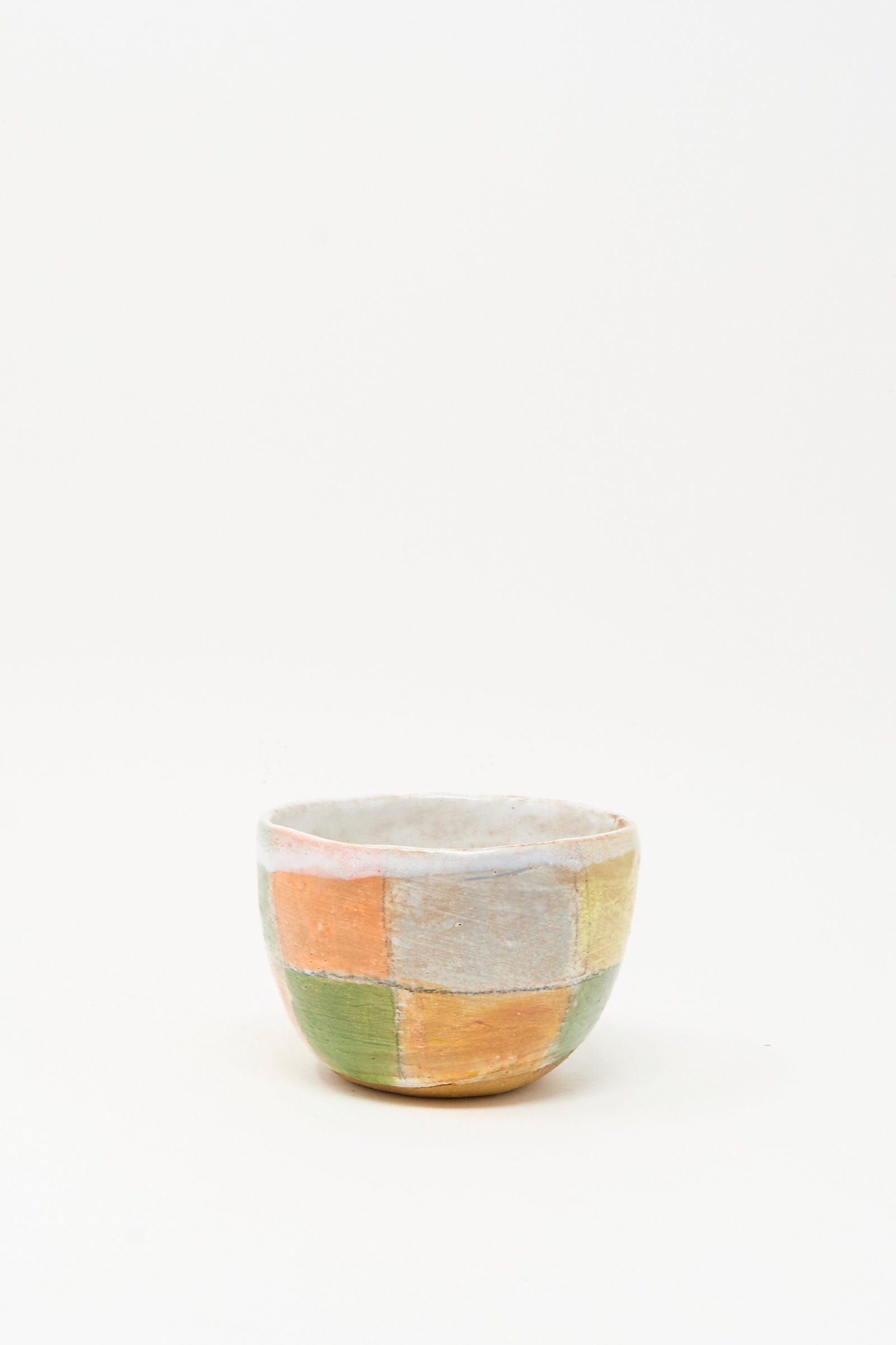 The Small Bowl in Check Multi II by Shino Takeda is a hand-painted ceramic bowl with a patchwork of muted orange, green, and cream squares, handmade in New York and photographed on a plain white background.