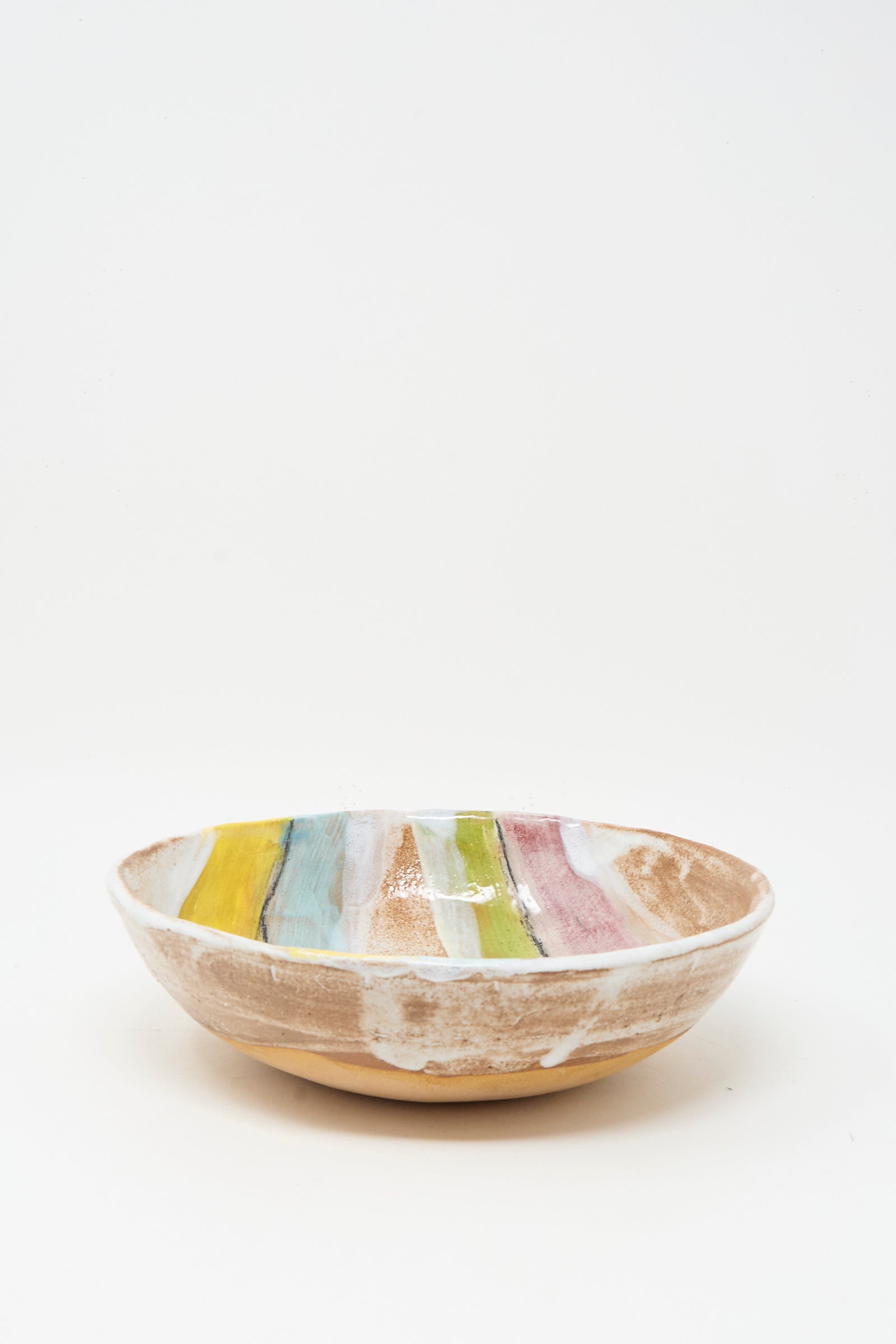The Stripe Serving Bowl in Multi II by Shino Takeda is a shallow ceramic bowl with a matte finish and striped pastel glaze inside, handcrafted in New York and displayed on a crisp white background.