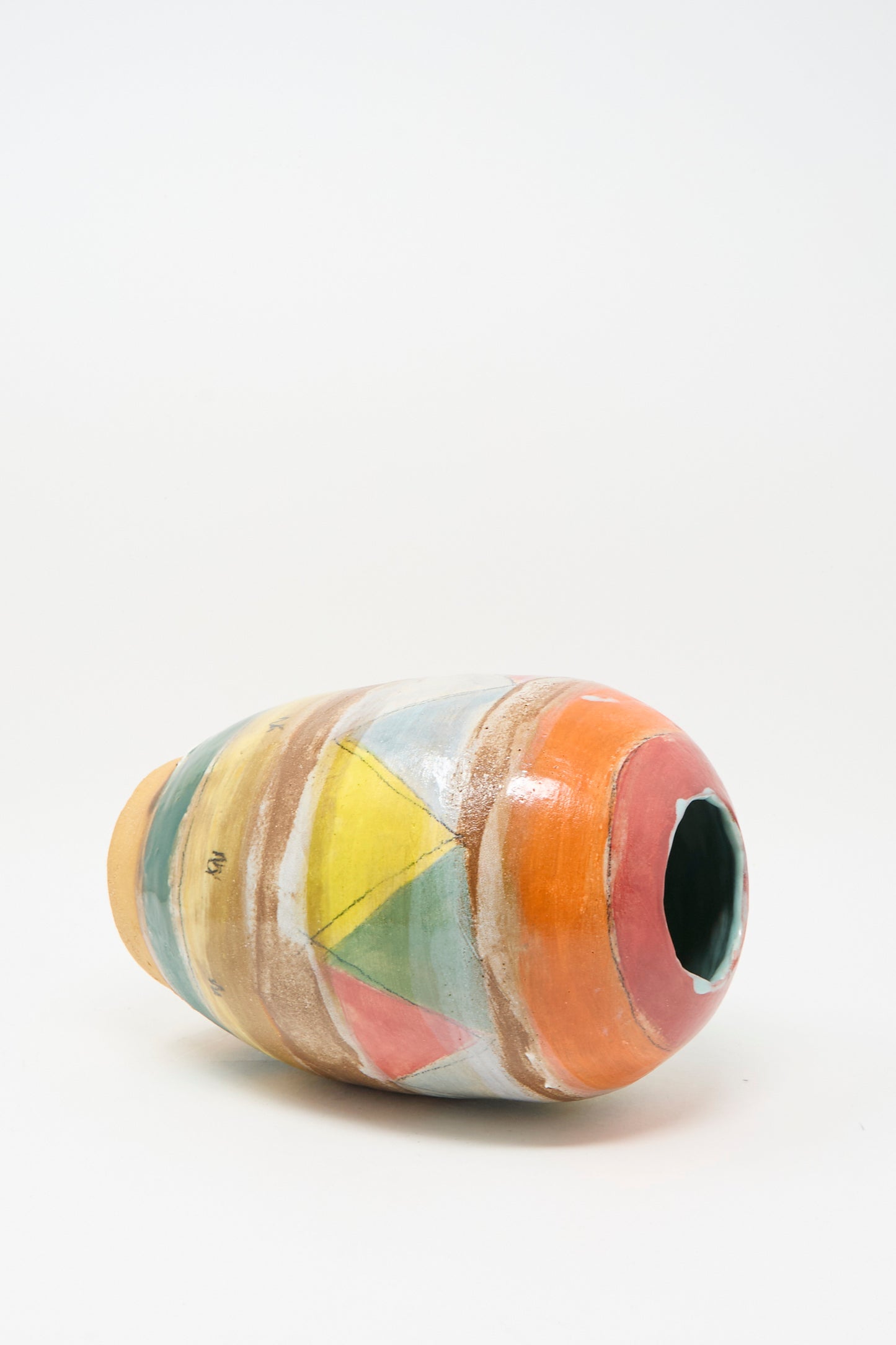 The Triangle Vase in Multi by Shino Takeda, a handmade clay vase with a wide opening and vibrant geometric designs in orange, yellow, green, and blue, lies on its side against a white background.