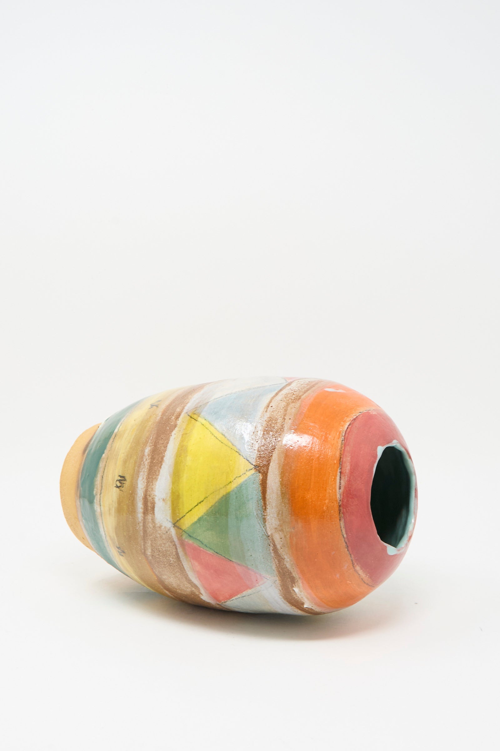 The Triangle Vase in Multi by Shino Takeda, a handmade clay vase with a wide opening and vibrant geometric designs in orange, yellow, green, and blue, lies on its side against a white background.