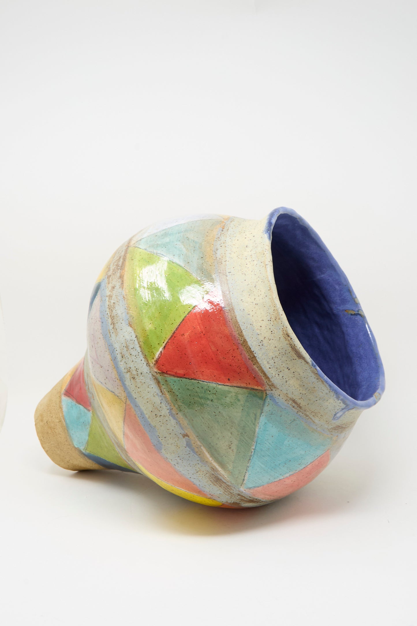 The Triangles Large Vessel in Multi by Shino Takeda is a handmade clay vase with a wide blue-rimmed opening and geometric shapes in vibrant colors, shown lying on its side against a white background.