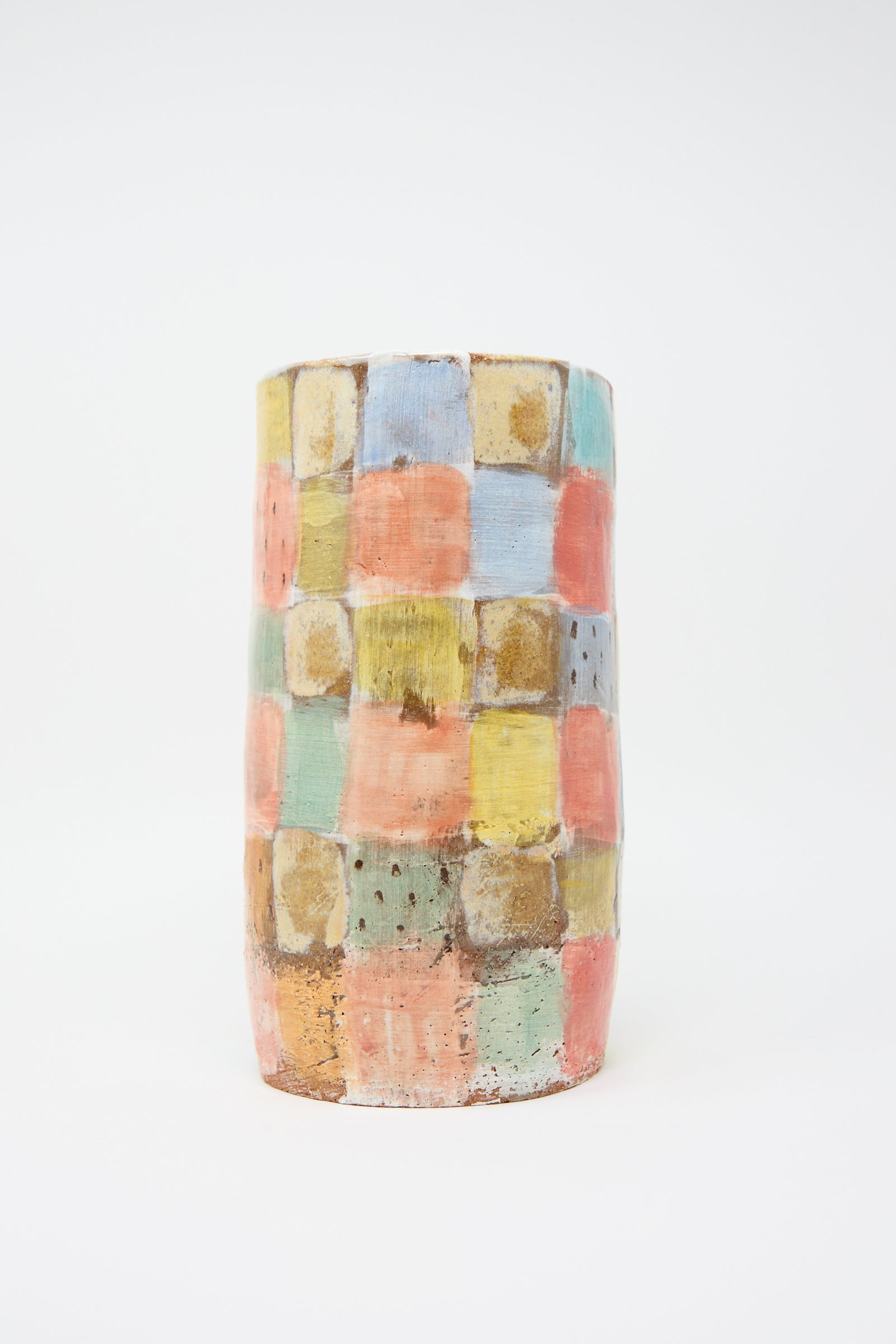 The "Vase in Pastel Checker" by Shino Takeda is a cylindrical, hand-painted ceramic piece in a checkered pattern of pastel colors—blue, pink, green, and yellow—set against a white background.