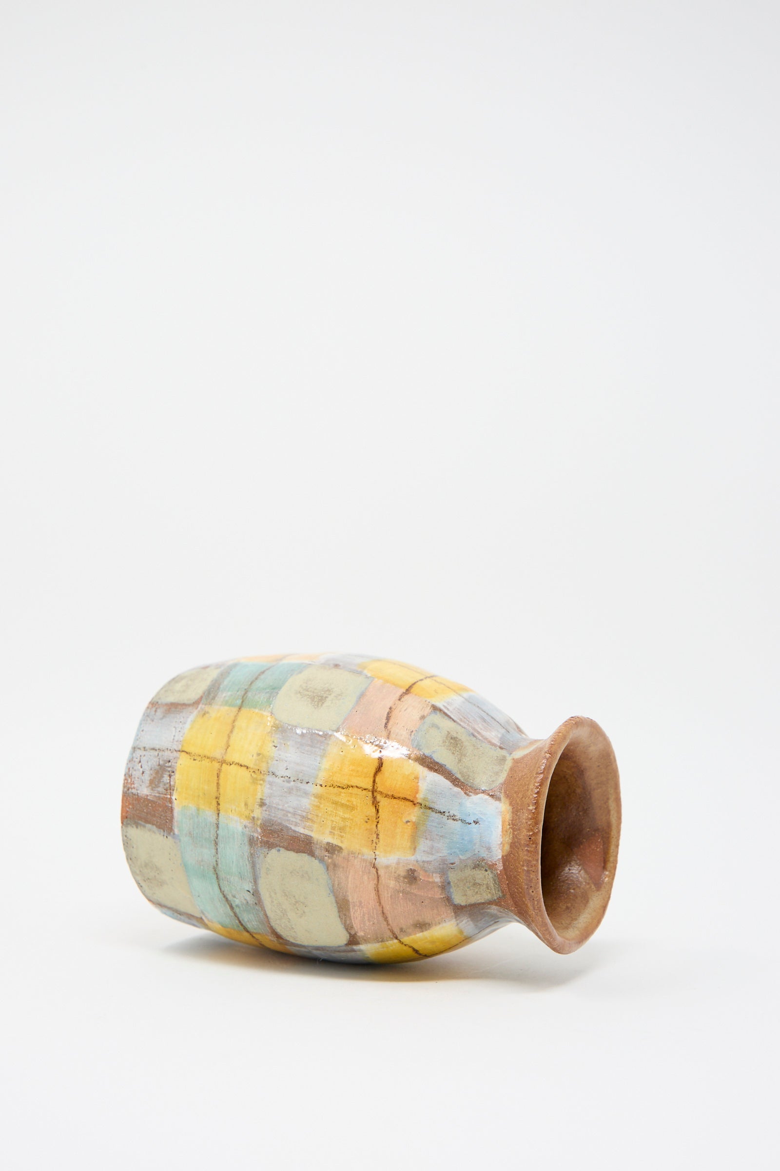 A hand-painted ceramic vase from Shino Takeda, named "Vase in Pastel Plaid," is displayed on its side against a simple backdrop.