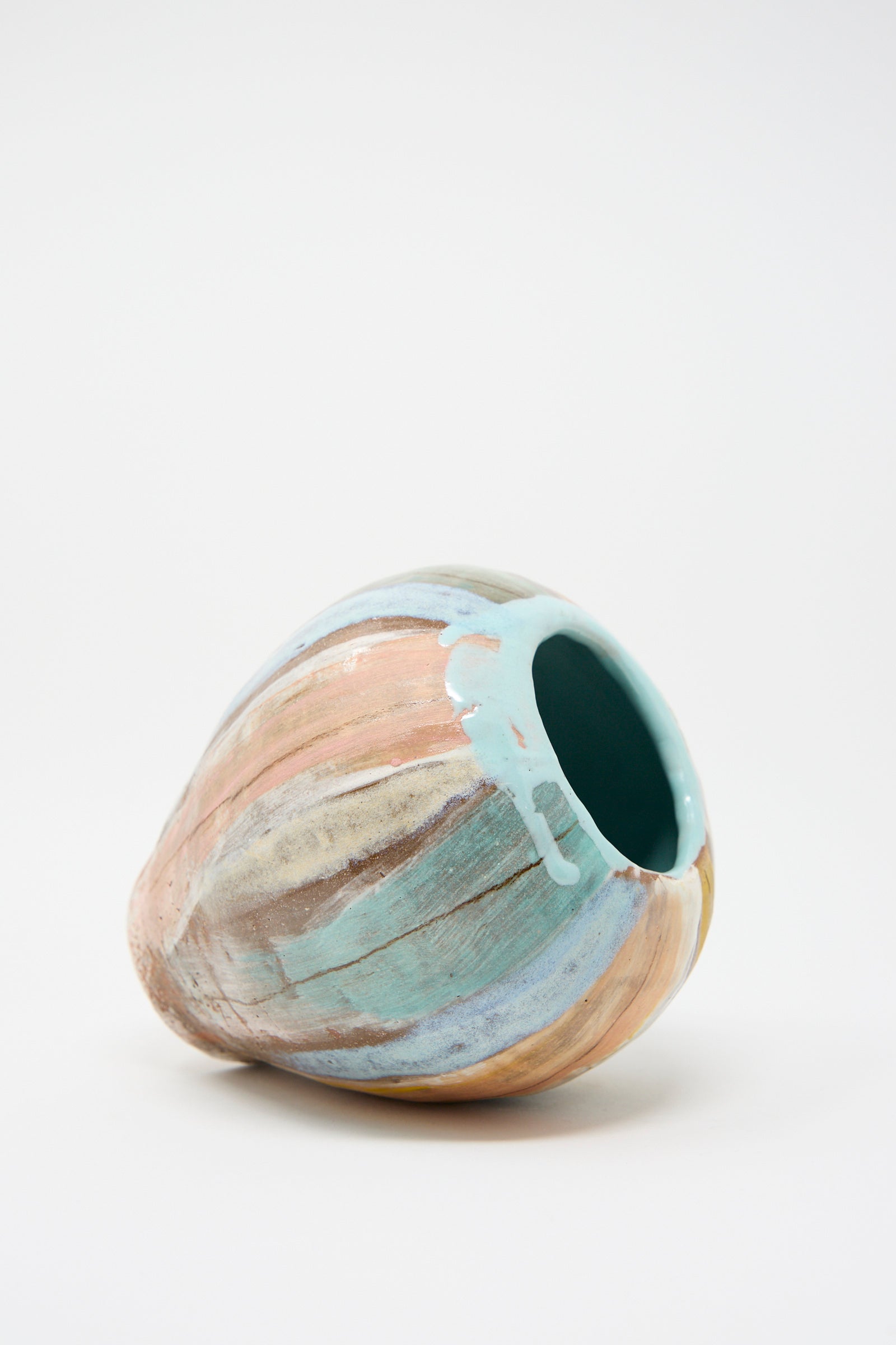 The Vase in Pastel Stripe by Shino Takeda, a hand-painted ceramic piece featuring multicolored pastel shades, lays on its side.