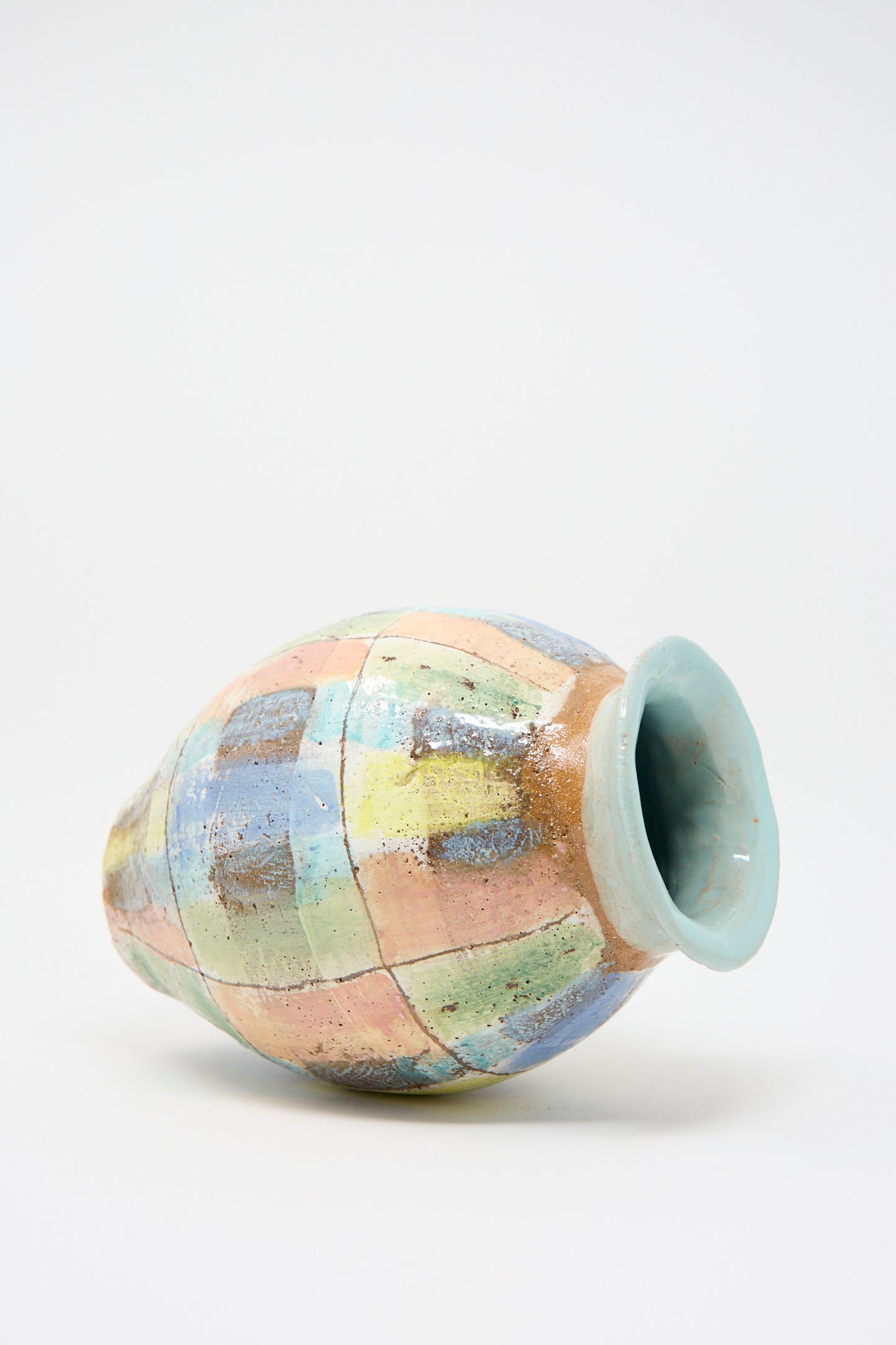 A ceramic object from Shino Takeda, the Vase in Pastel Plaid with Blue, lies on its side.