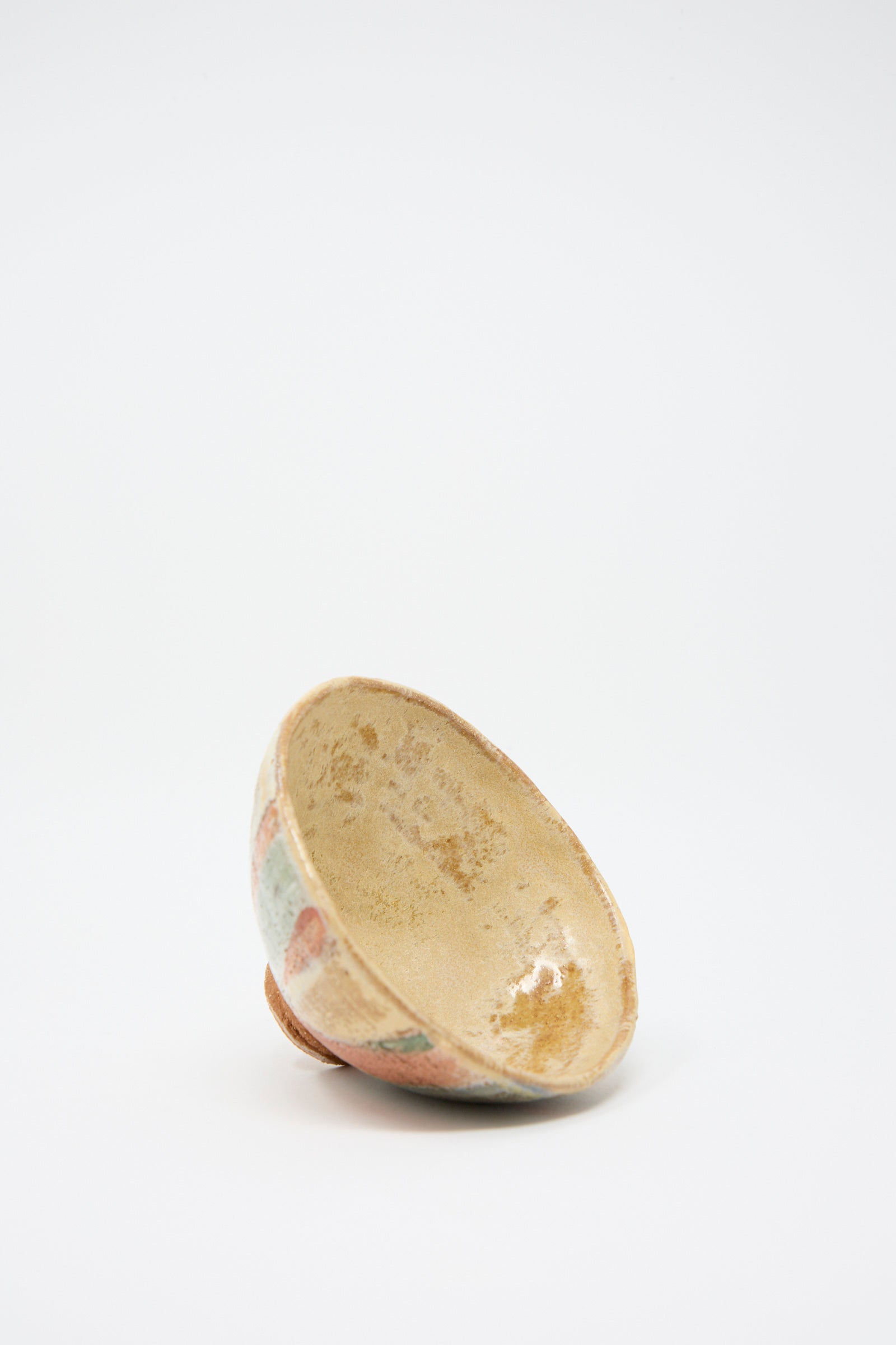 Resting on its side against a plain white background is a small, weathered Footed Bowl in Pastel Stripe by Shino Takeda, featuring a light brown and faded hand-painted pattern.