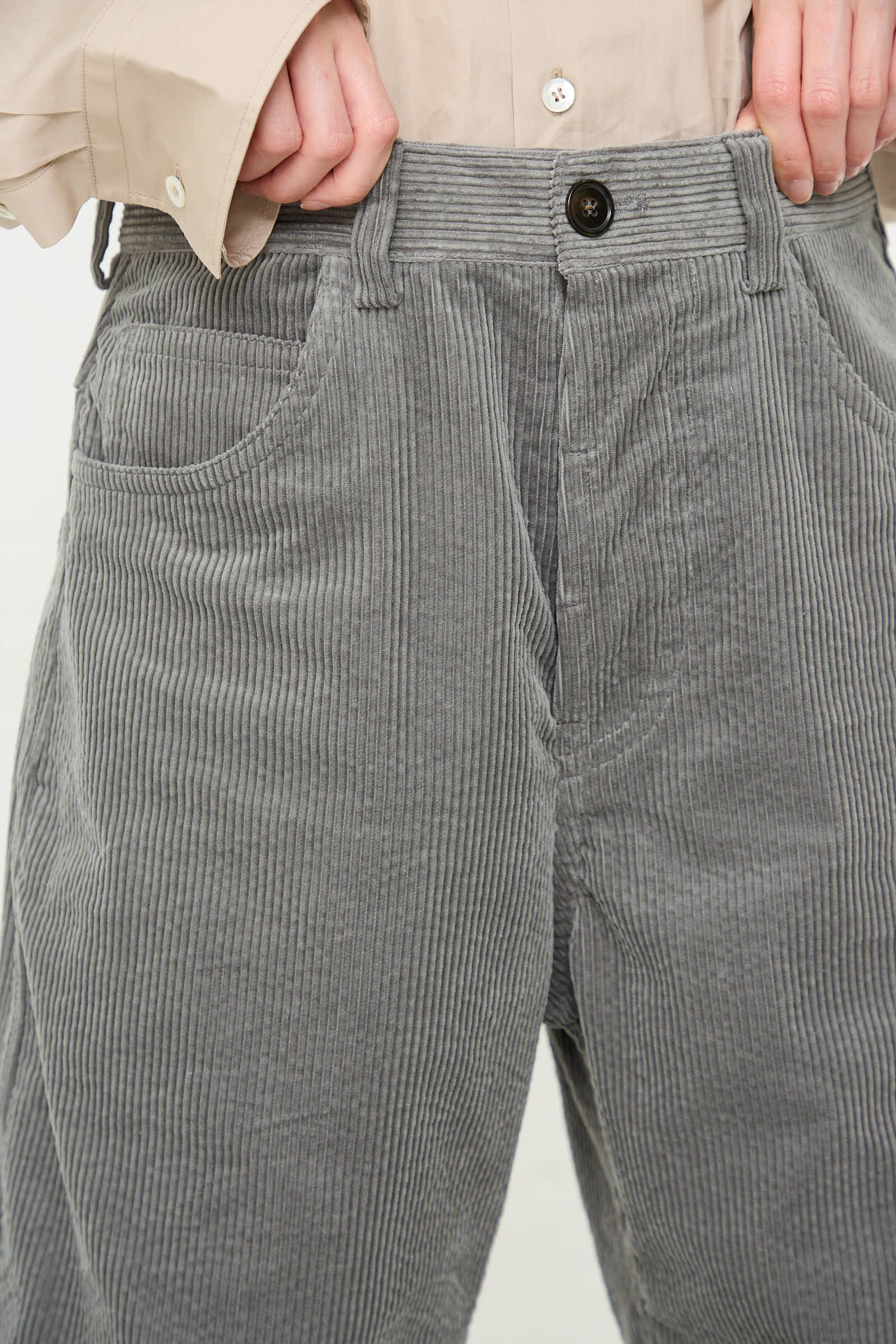 Close-up of a person wearing Sofie D'Hoore's Cotton Corduroy Pavia Pant in Sage, paired with a light beige button-up shirt, with their hands placed near their waist.