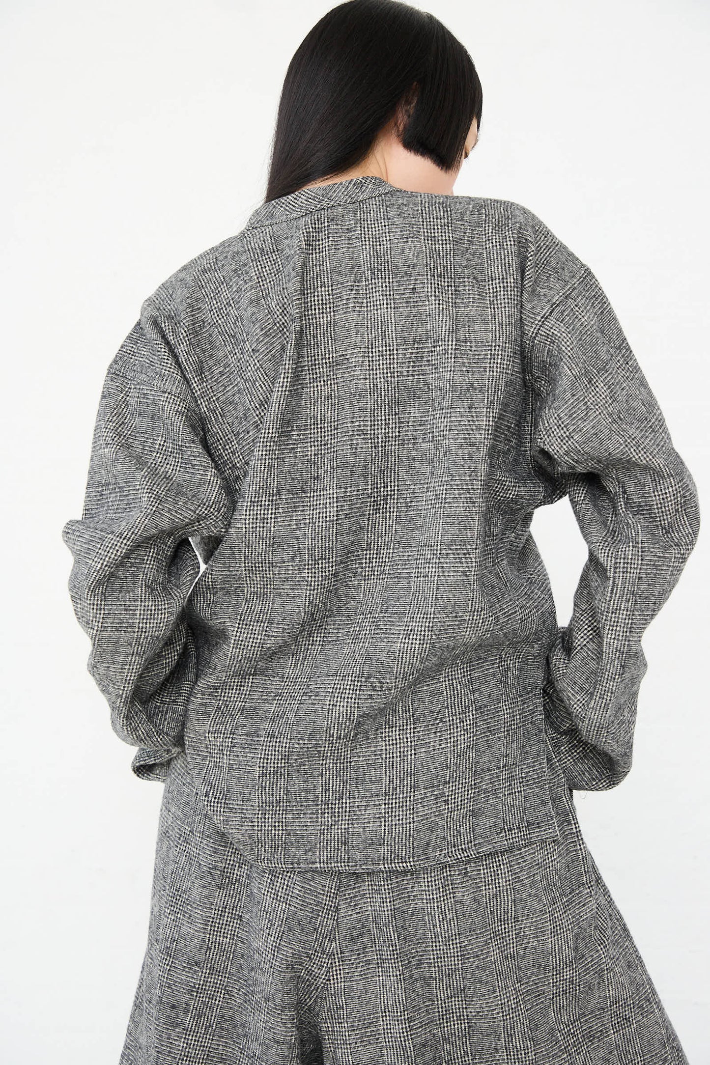 A person with long black hair is seen from the back, wearing a Sofie D'Hoore Cotton Wool Washed Biba Top in Mid Grey and matching pants. The background is plain white.