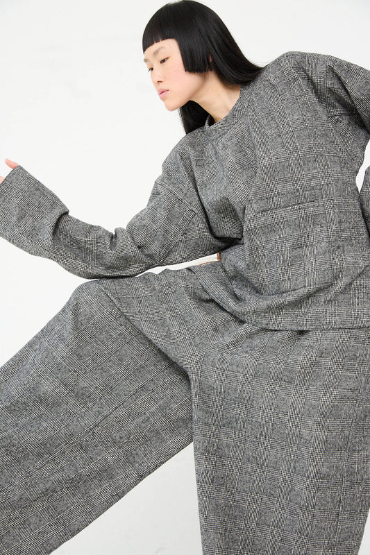 Person with long black hair wearing a matching tonal grey plaid outfit, featuring Sofie D'Hoore's Cotton Wool Washed Palau Pant in Mid Grey, poses with arms and legs extended in a dynamic stance.