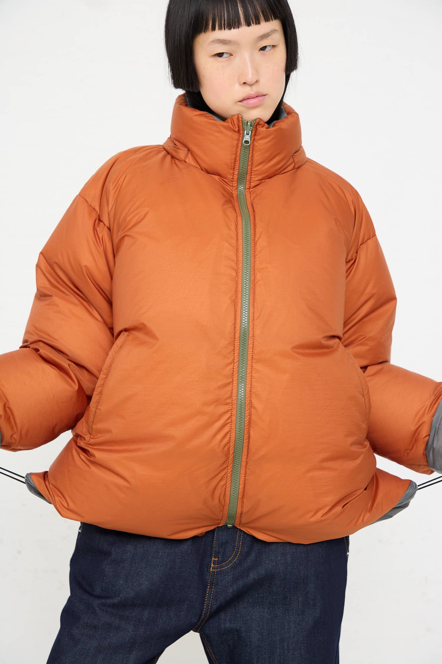 Person wearing a Sofie D'Hoore Down Filled Odna Reversible Jacket in Rust and Sage, posing against a white background.