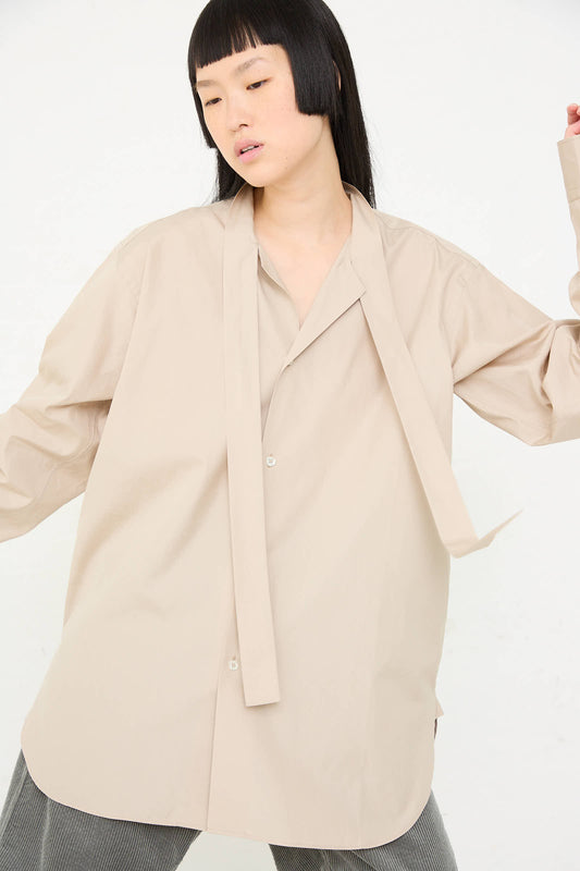 A person wearing a loose-fitting Paper Touch Poplin Bow Shirt in Stone by Sofie D'Hoore poses against a plain white background.