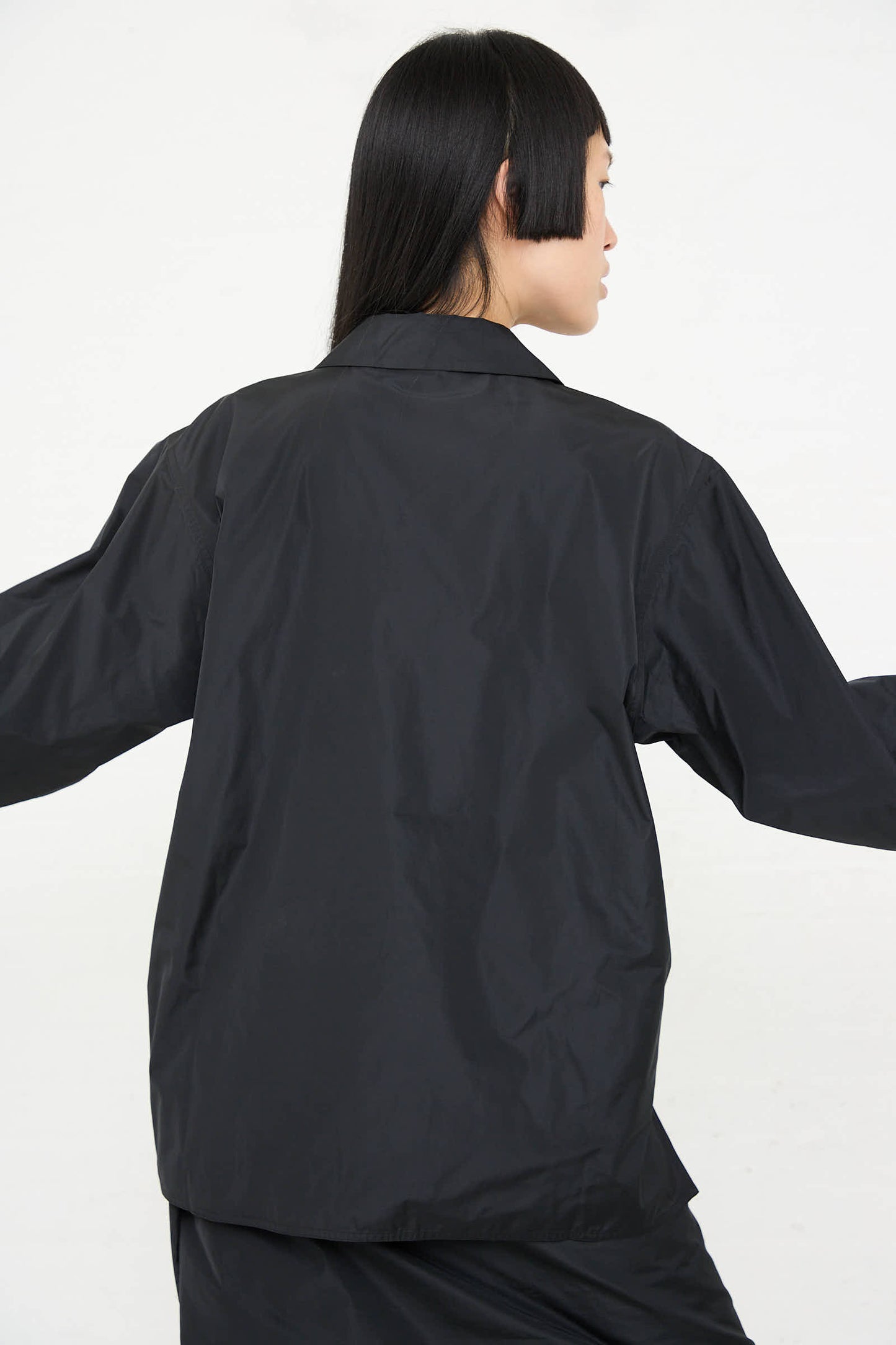 A person with shoulder-length hair is shown from the back, wearing a relaxed fit, black Taffeta Barry Shirt with Patch Pocket by Sofie D'Hoore, against a white background.